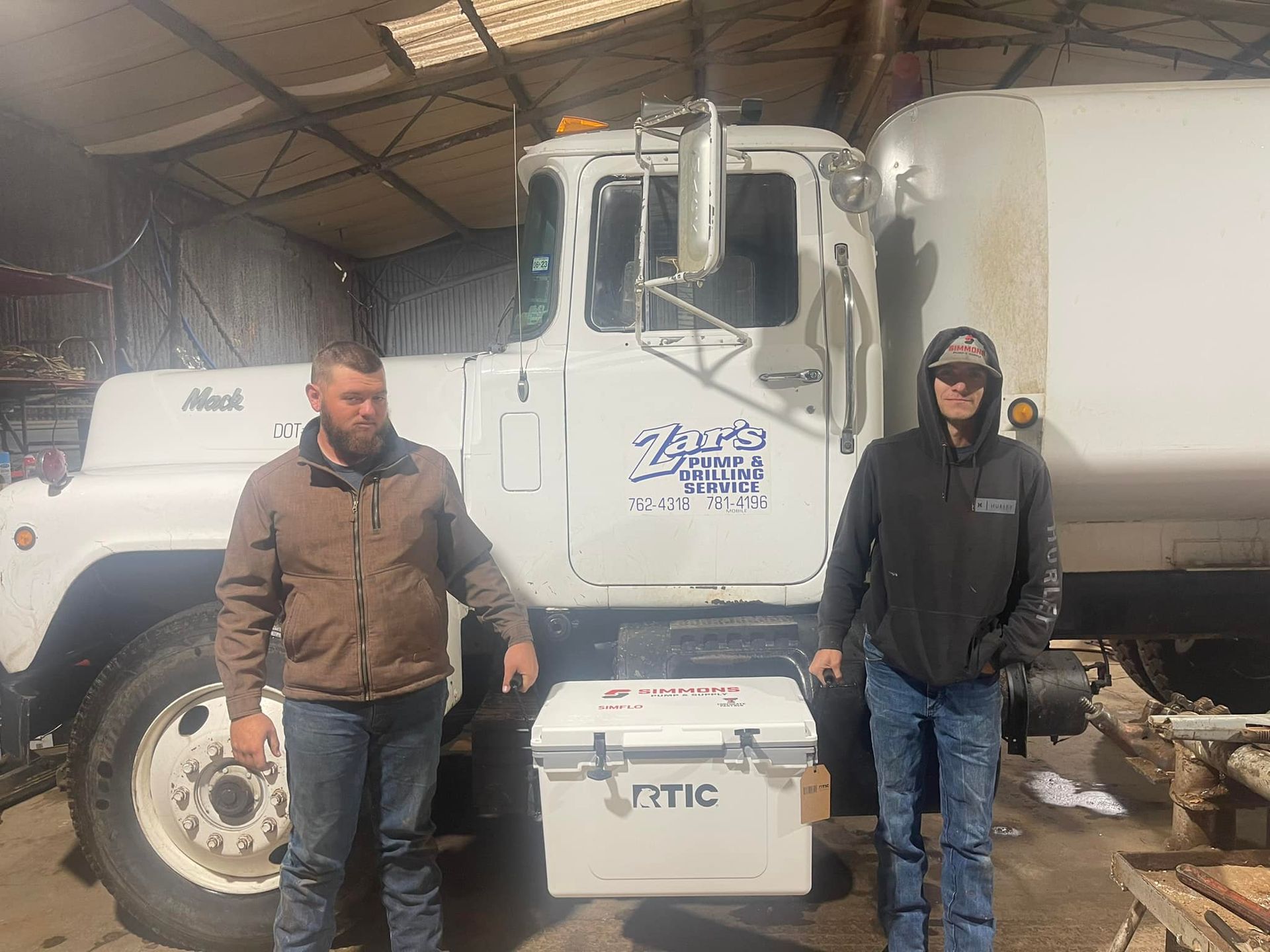 Two people standing beside a white utility truck inside a warehouse, with a cooler in front.