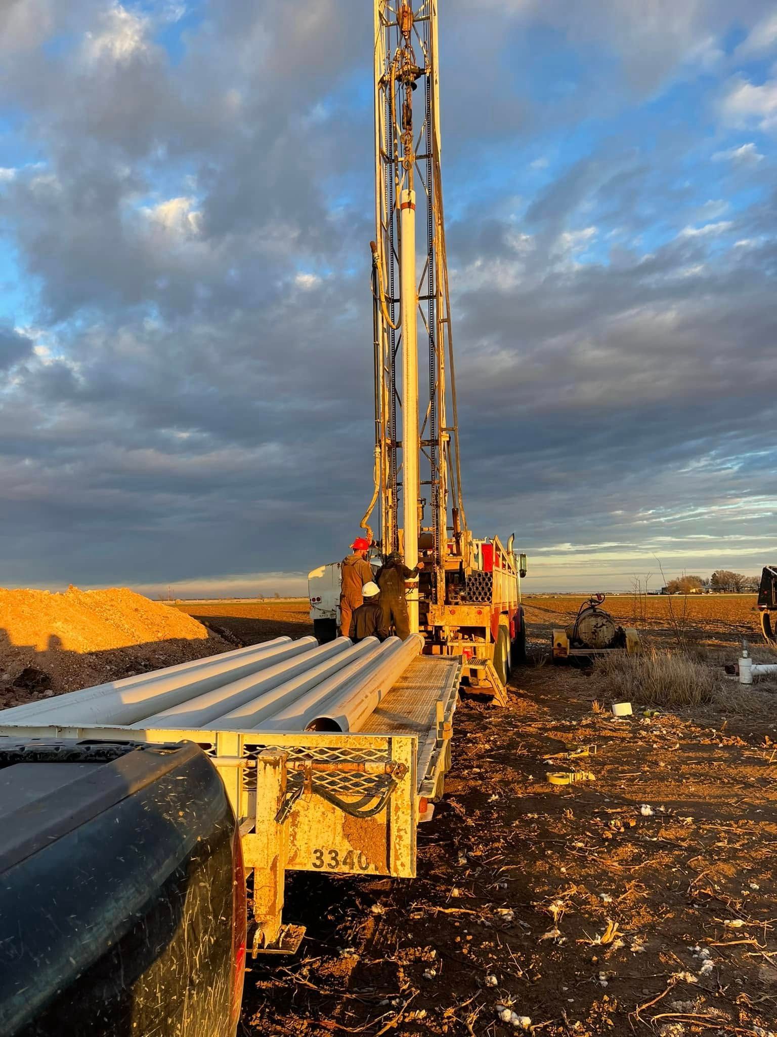 Drilling rig on a muddy construction site under a cloudy sky, with pipes in the foreground.