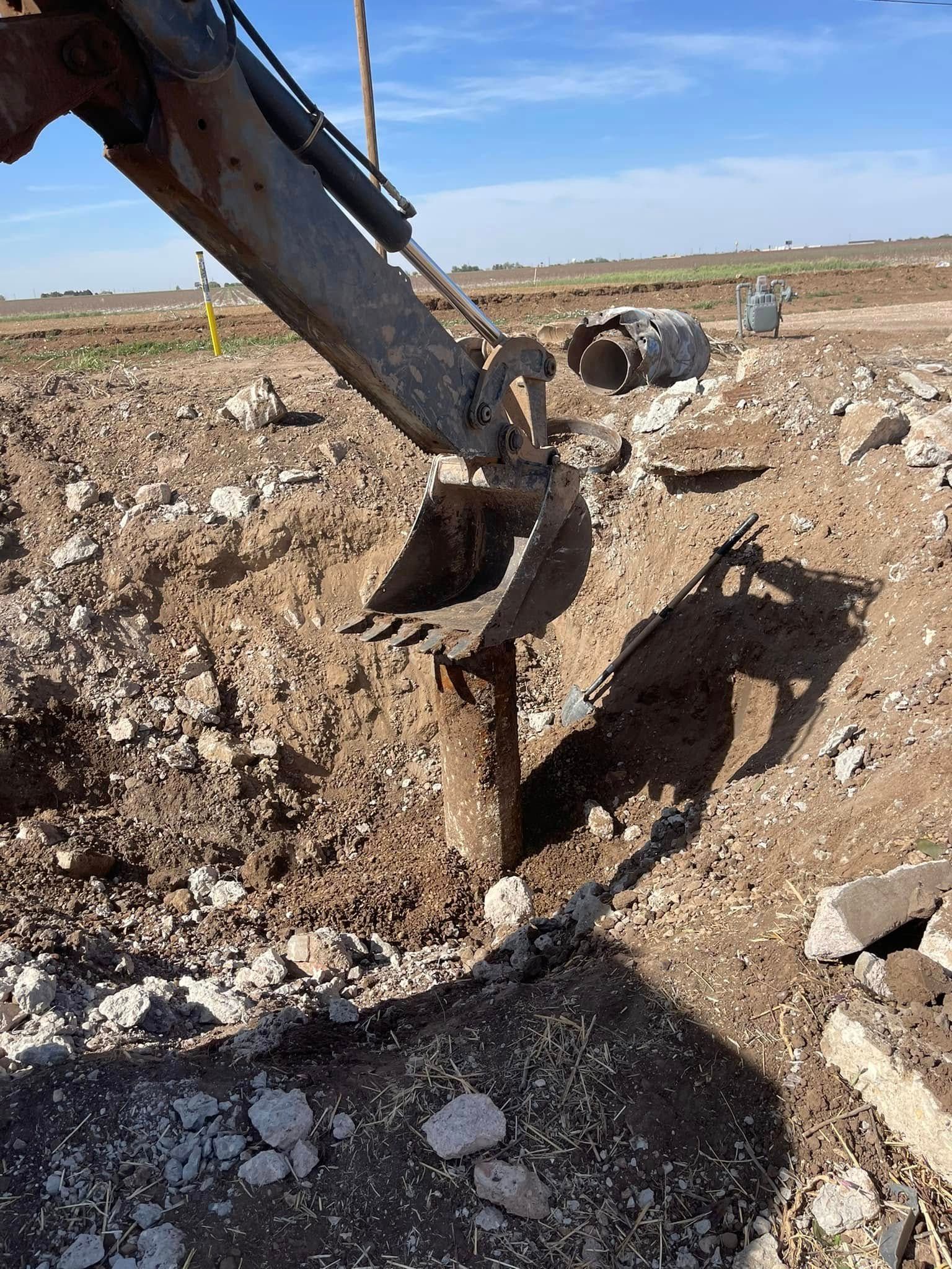 Excavator bucket digging into rocky ground on a construction site under a clear sky