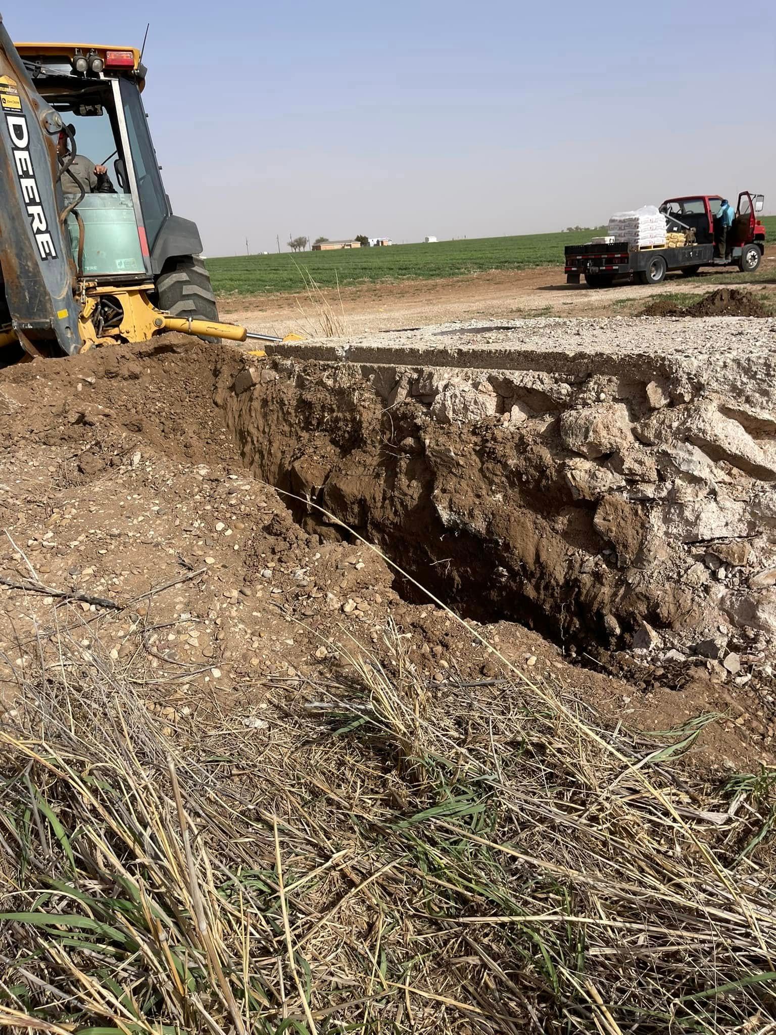 Excavator digging a deep trench in a muddy farm field, with a truck in the distance.