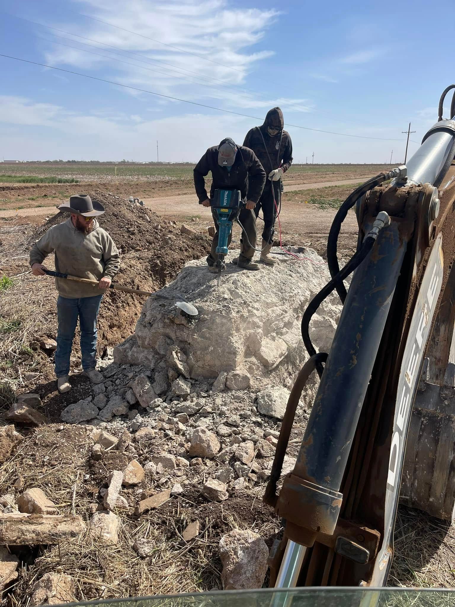 People standing on rocky terrain near a large metal machine arm under a blue sky