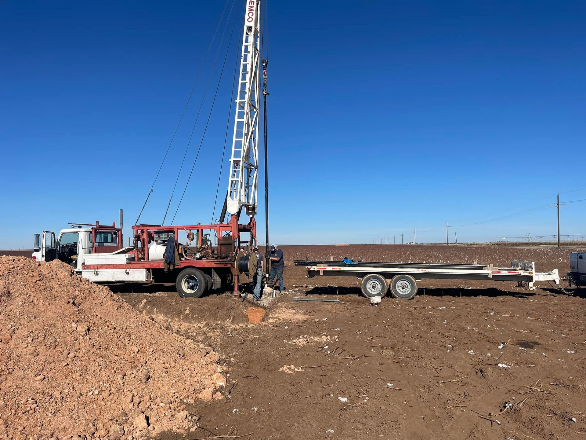 Drilling rig truck beside a mound of dirt on a barren construction site under a blue sky