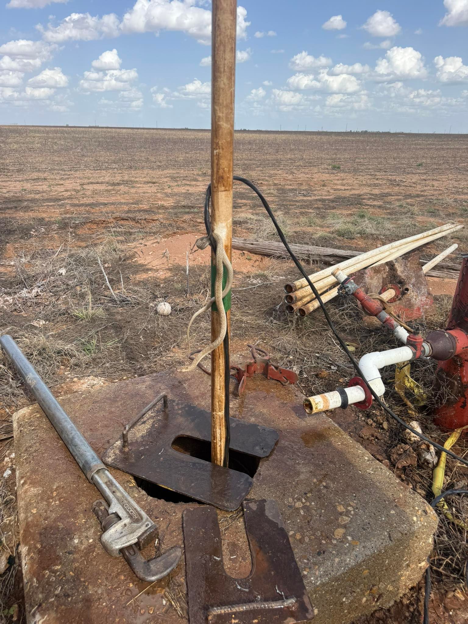 Rusty survey pole on a flat dirt field beside equipment under a cloudy sky.