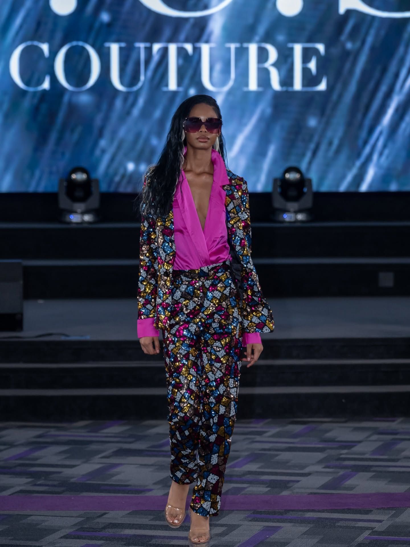 Fashion model in floral suit and pink blouse walking runway at couture show
