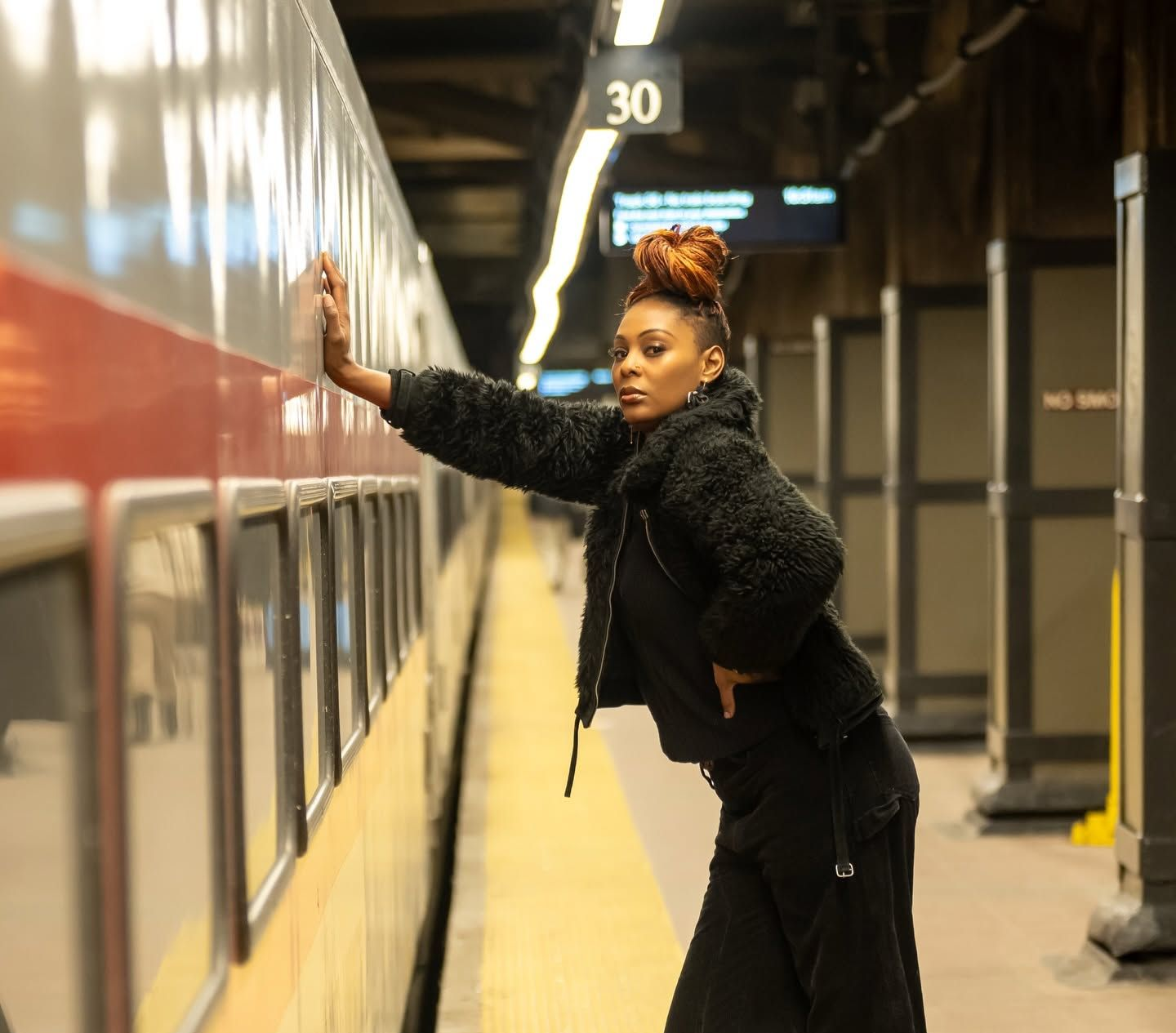 Person leaning against a train at a station platform, wearing black, with platform sign 30 above.