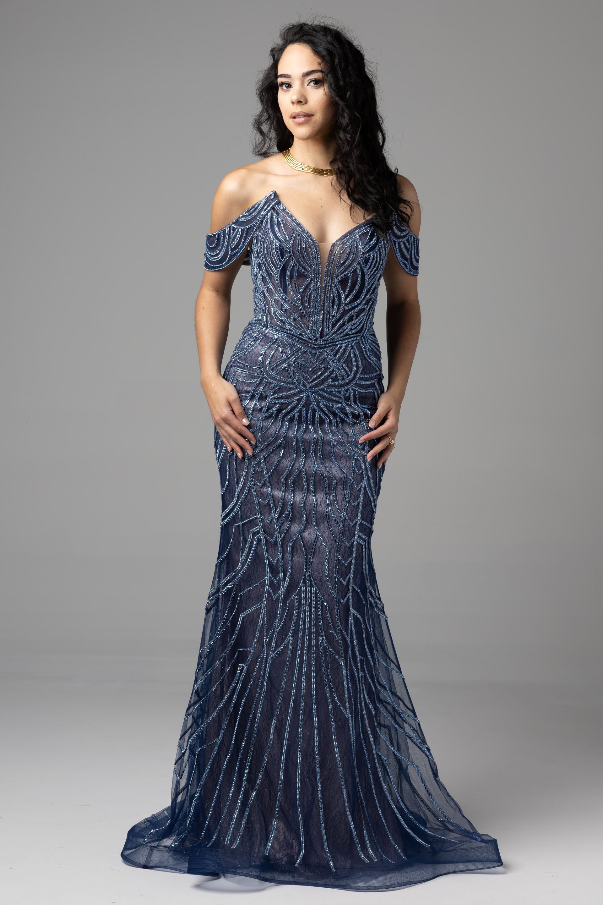 Woman in a navy sequined evening gown posing against a gray backdrop.