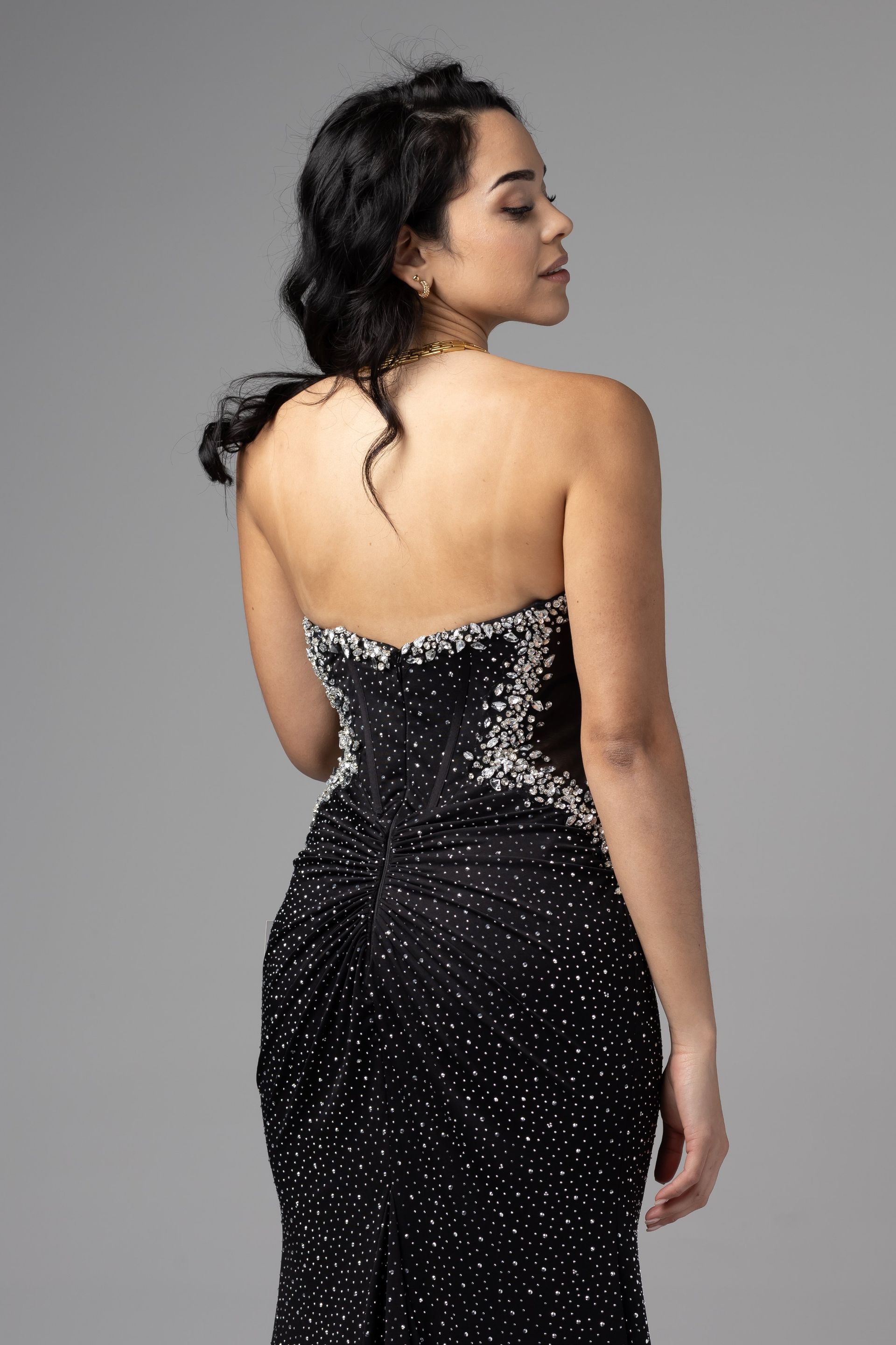 Woman in a black sequined strapless gown, shown from the back against a gray background.