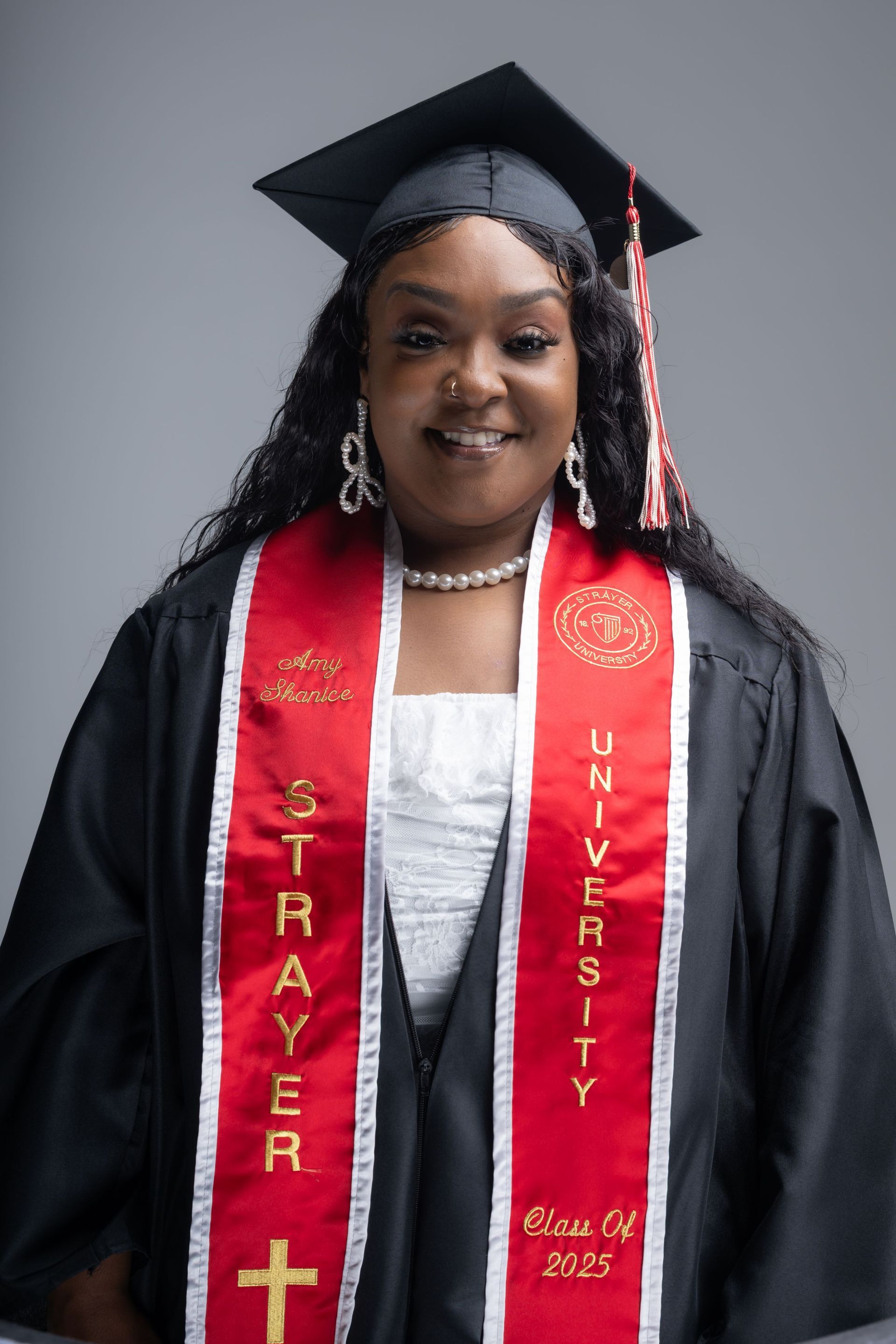 Graduate in cap and gown wearing red stole, smiling against a gray backdrop.