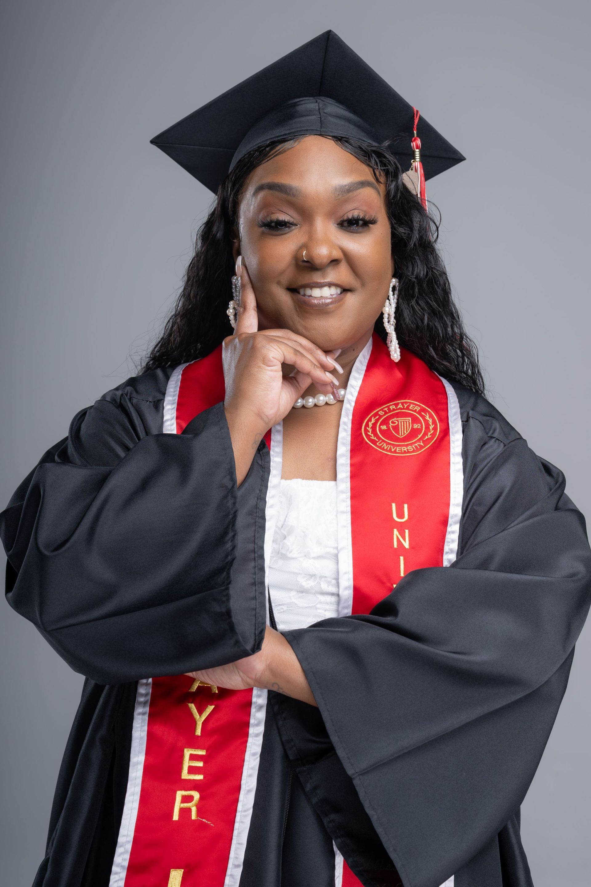 Graduation portrait of a smiling student in cap and gown with red stole against a gray background