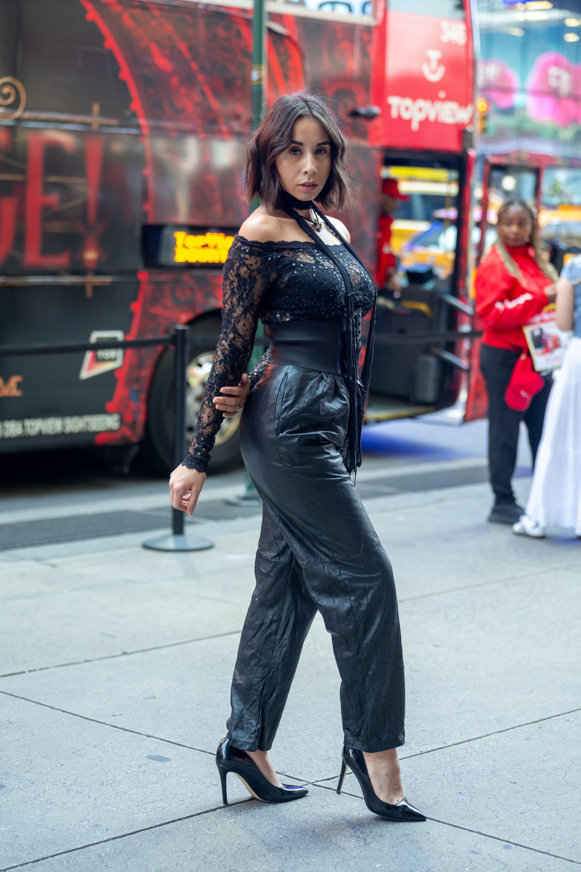 Person in black outfit and heels posing on a city street with colorful billboards in the background