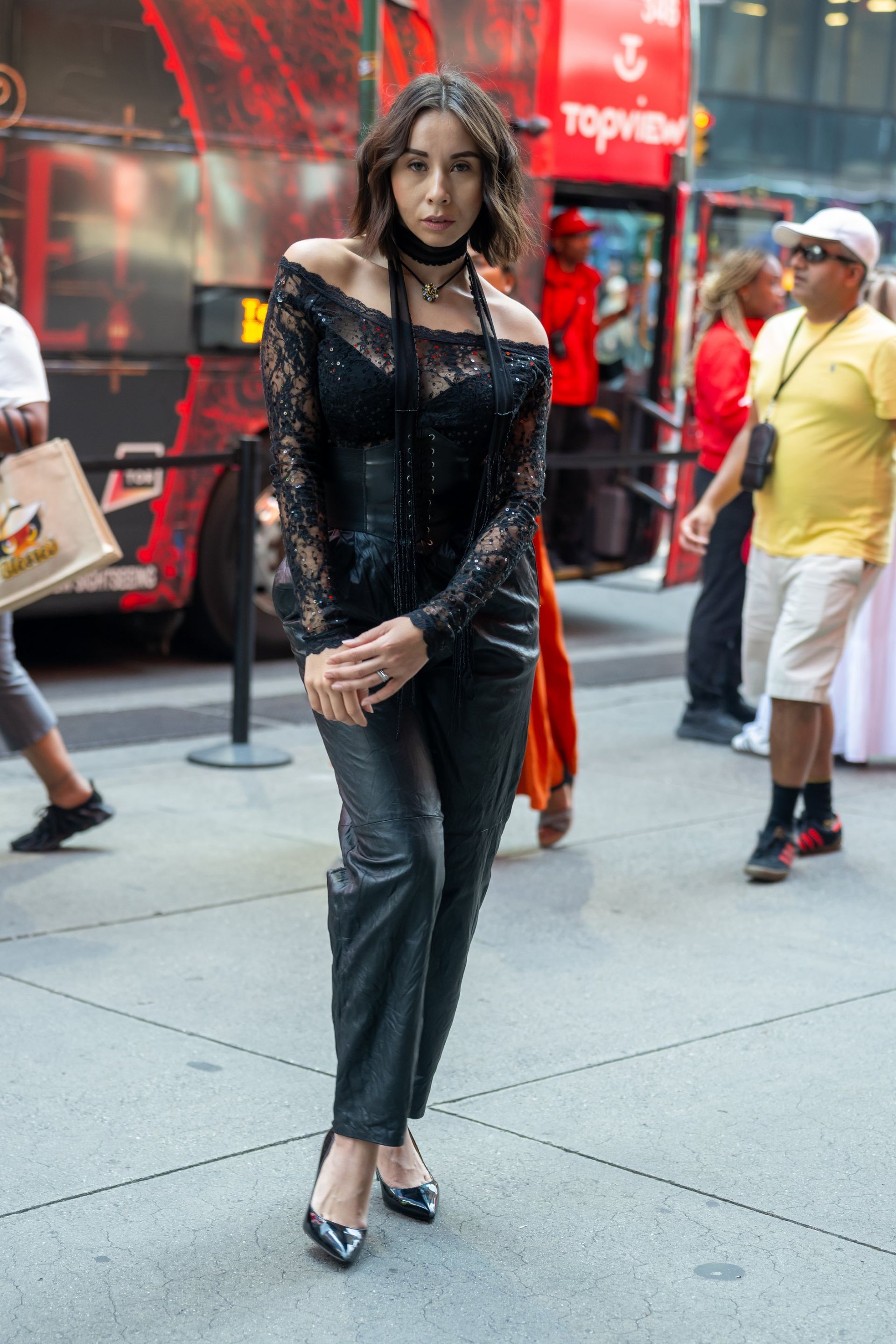 Person in black sequined top and gray pants standing on a city sidewalk.