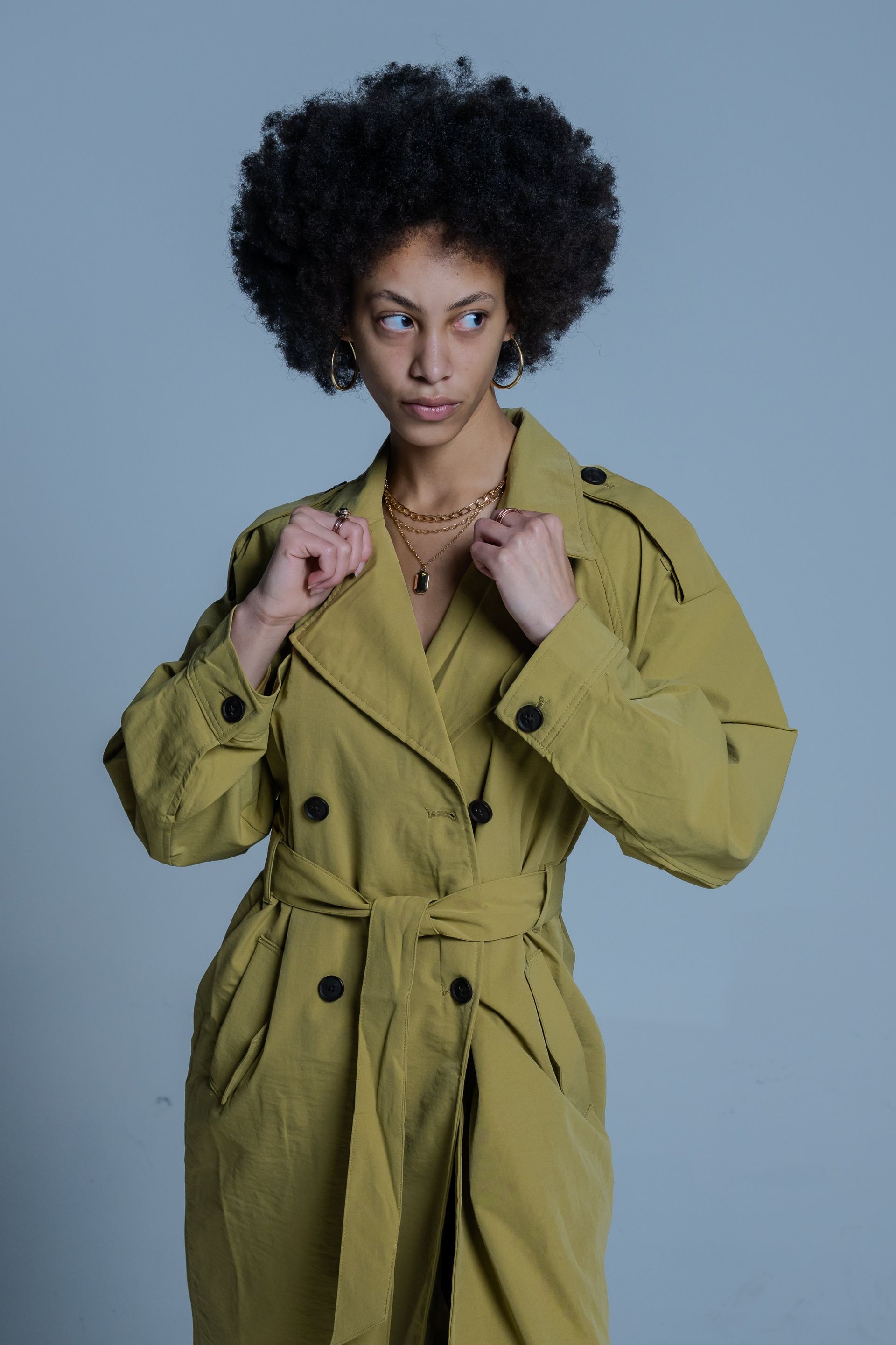 Person wearing an olive trench coat poses against a gray background.