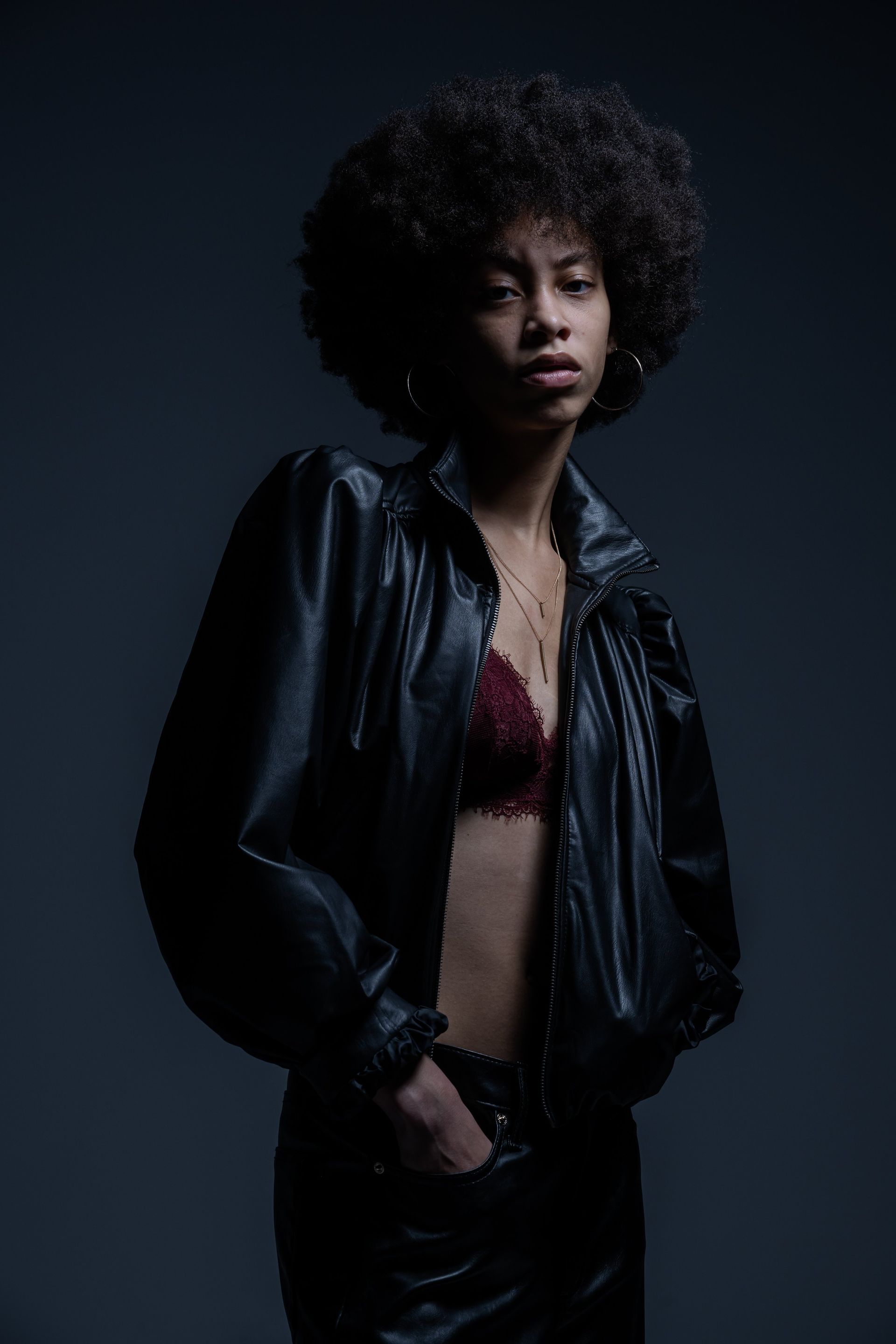 Person in a black leather jacket over a burgundy top against a dark studio background