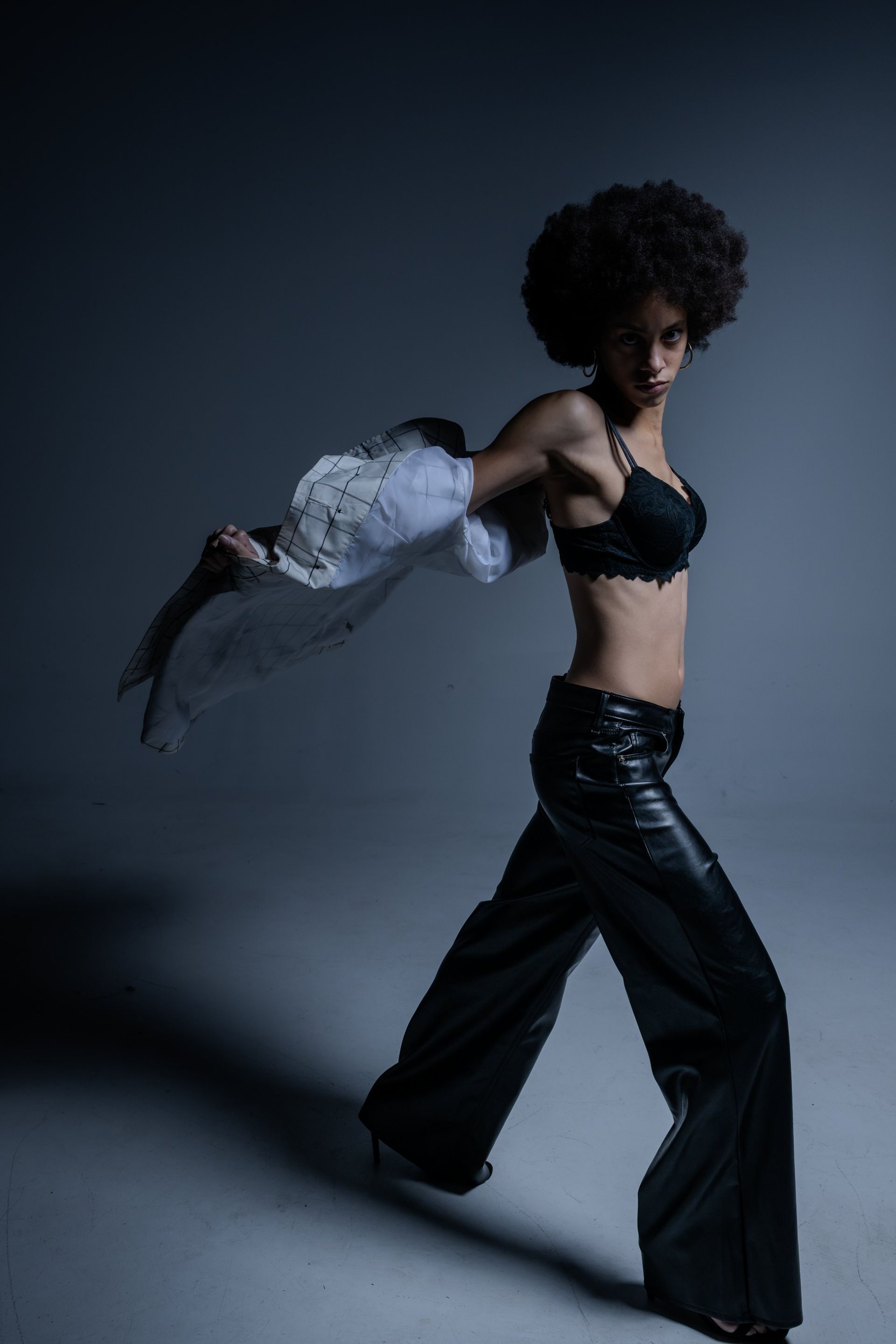 Fashion model in black outfit with sheer sleeves, posing against a dark studio backdrop.