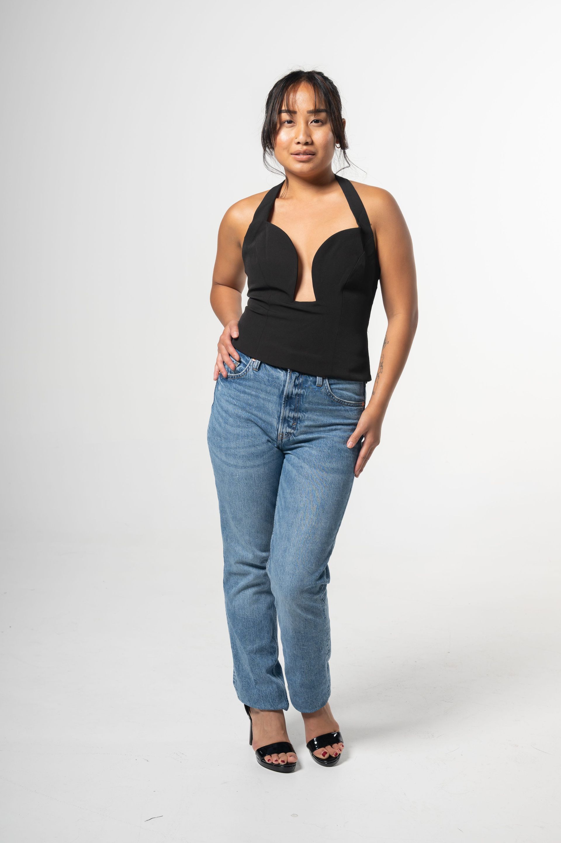 Person standing against a white backdrop in a black halter top, blue jeans, and black heels.