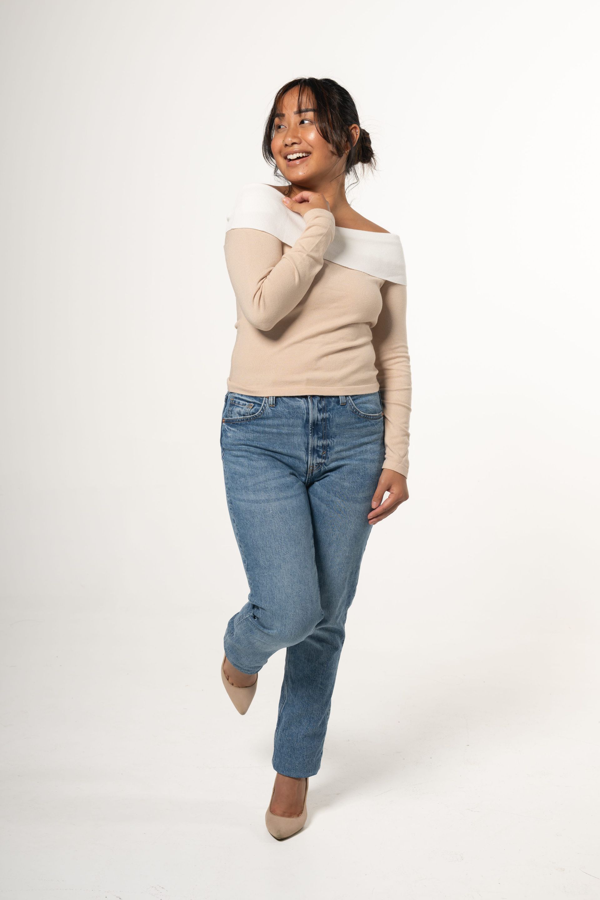 Woman posing in a beige top and blue jeans against a white studio background