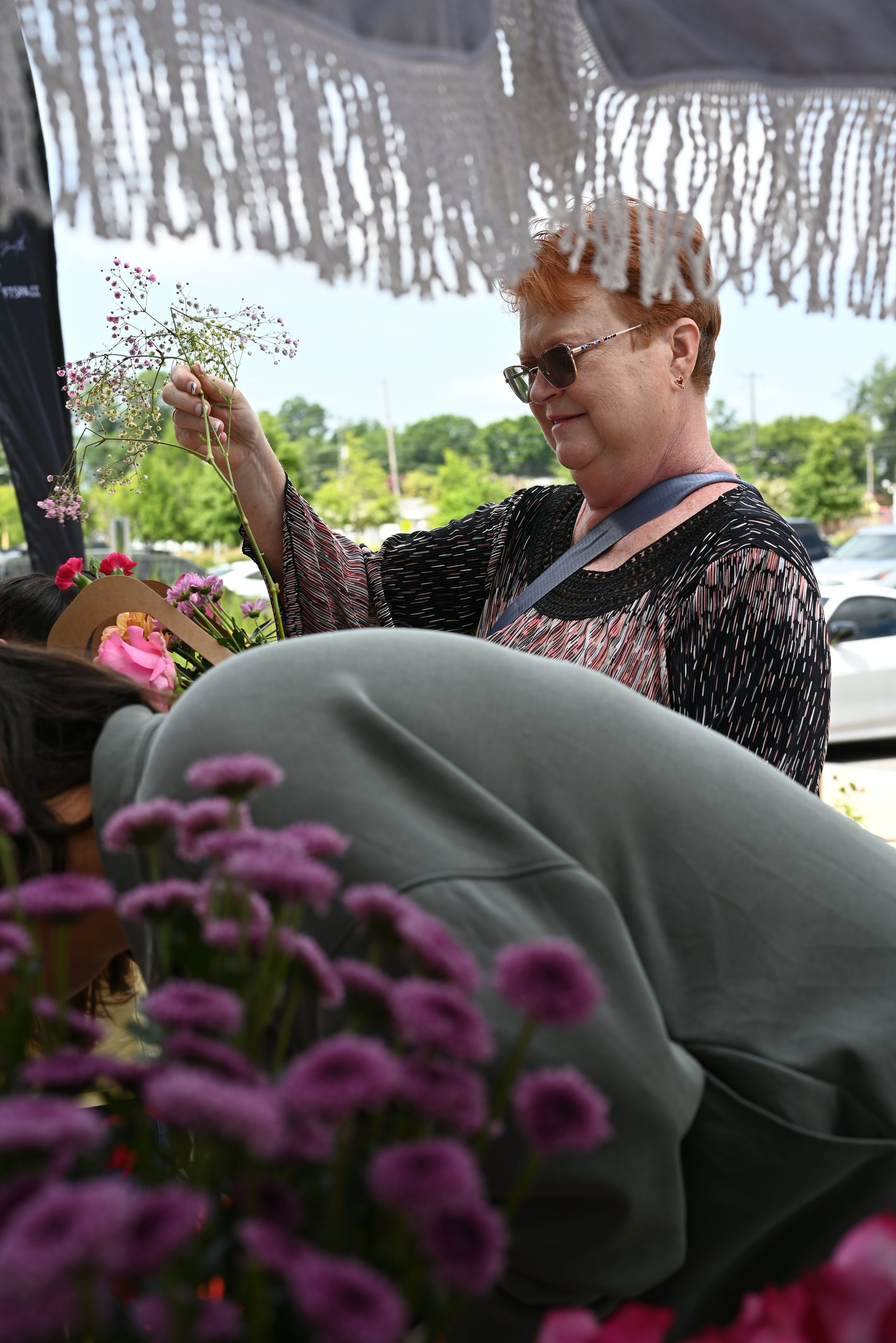 Woman in sunglasses standing under a canopy, holding flowers at an outdoor event.