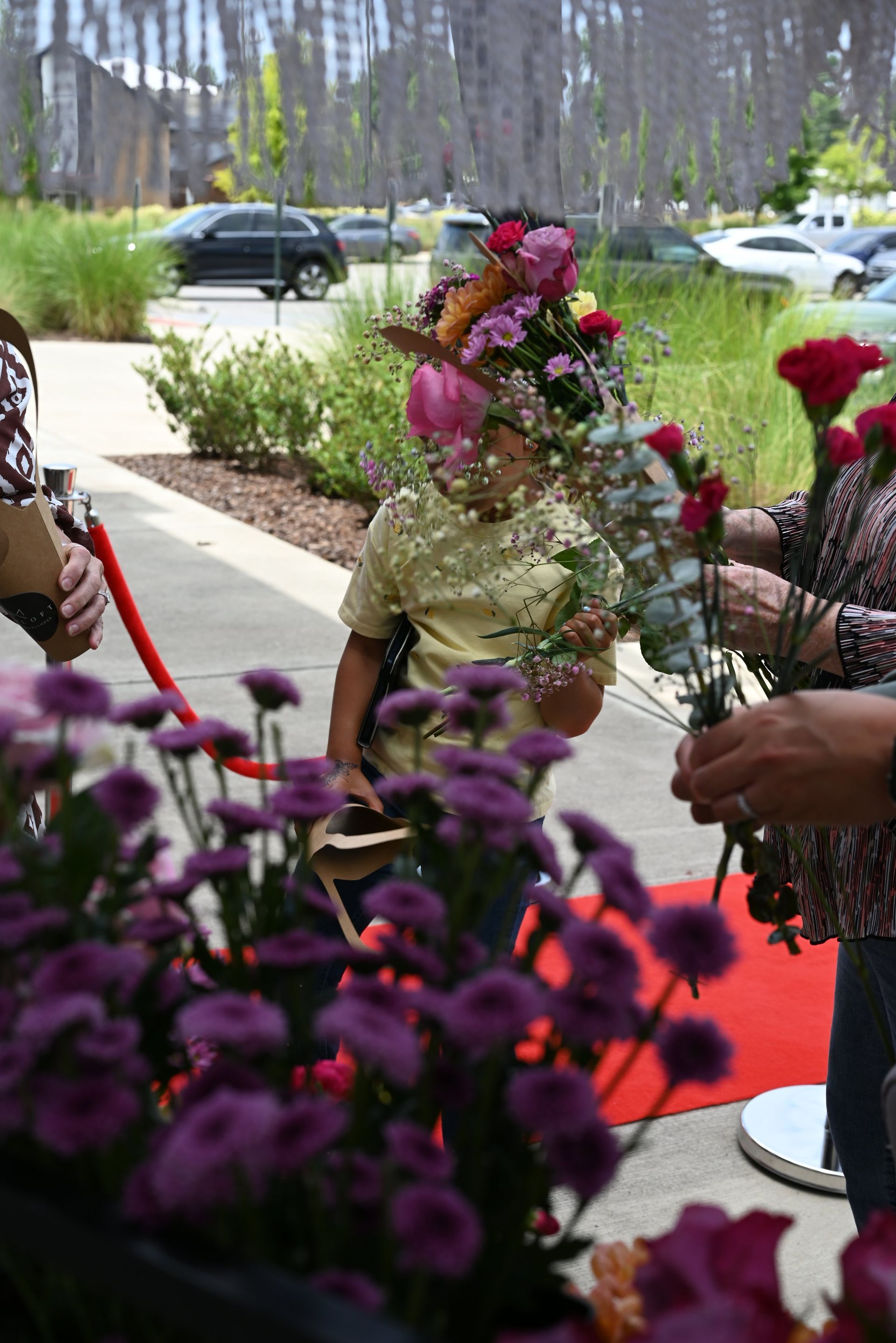 People arranging colorful flowers at an outdoor event with parked cars and trees in the background