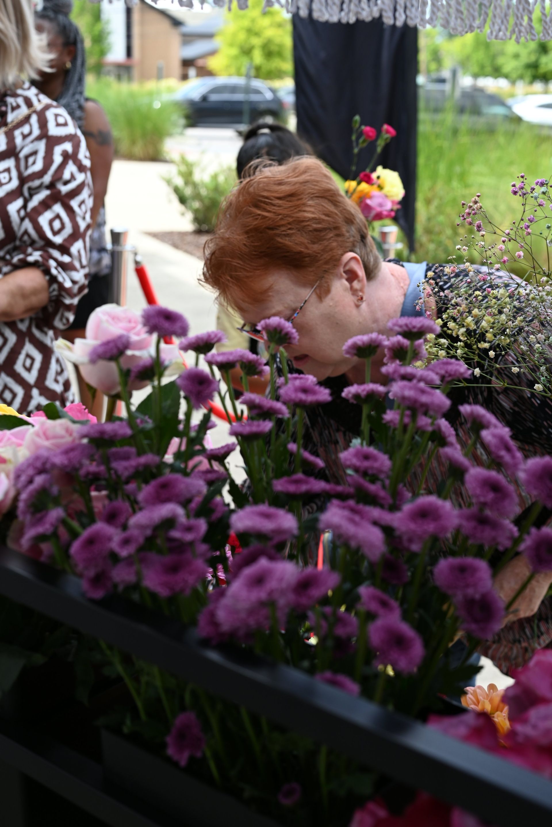 Person smelling purple flowers at an outdoor market stall