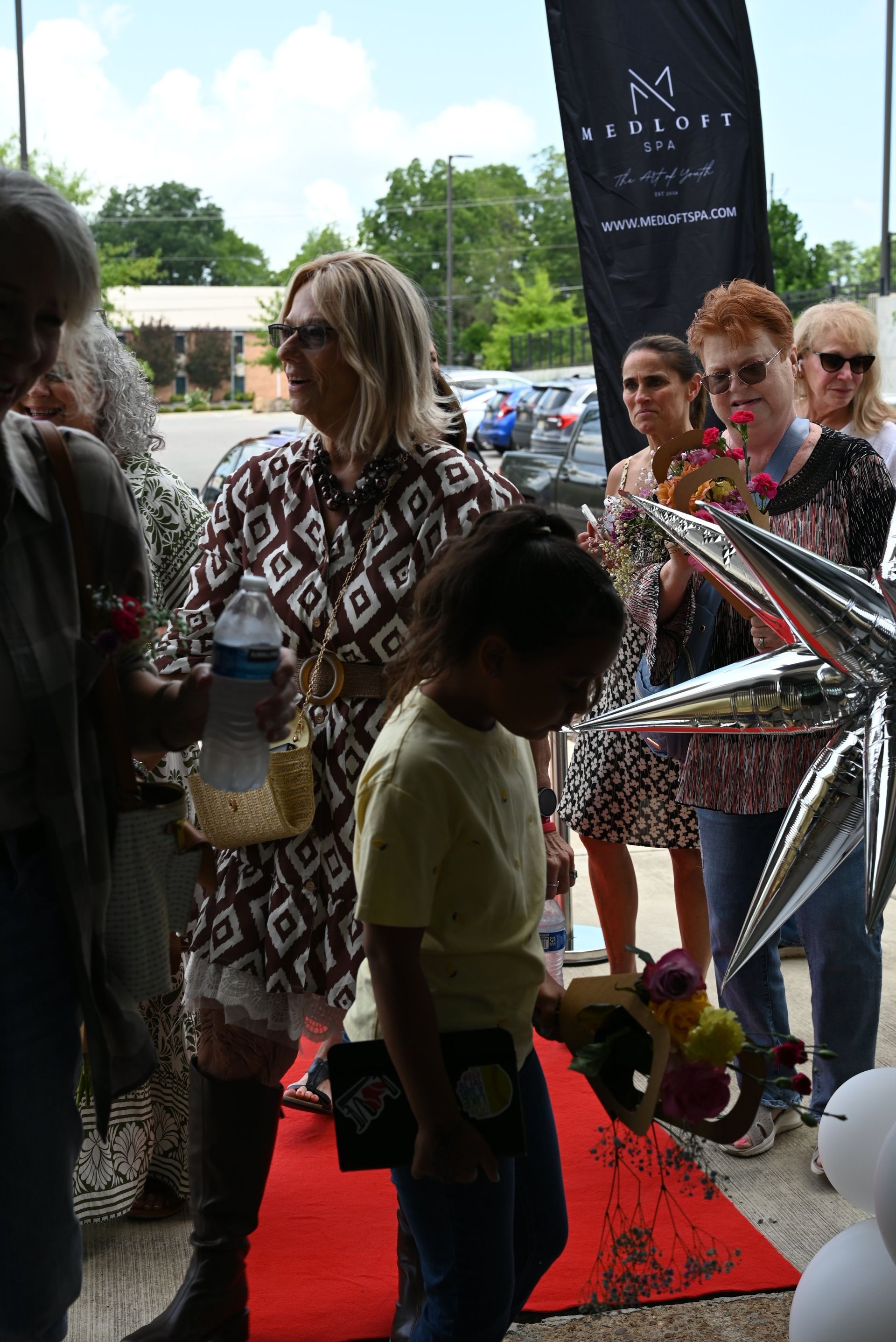 People standing on a red carpet at an outdoor event with a silver star decoration and black banner