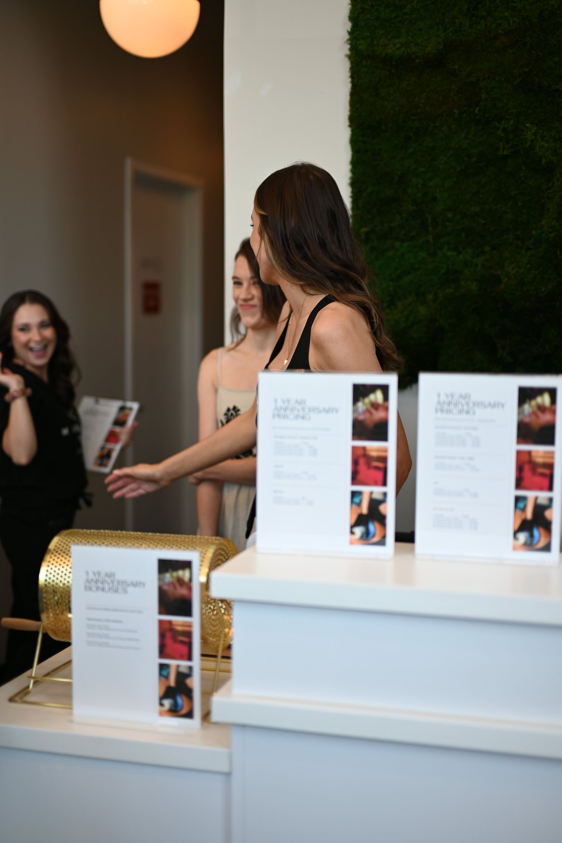 Two women speaking beside a white display table with brochures in a bright indoor lobby
