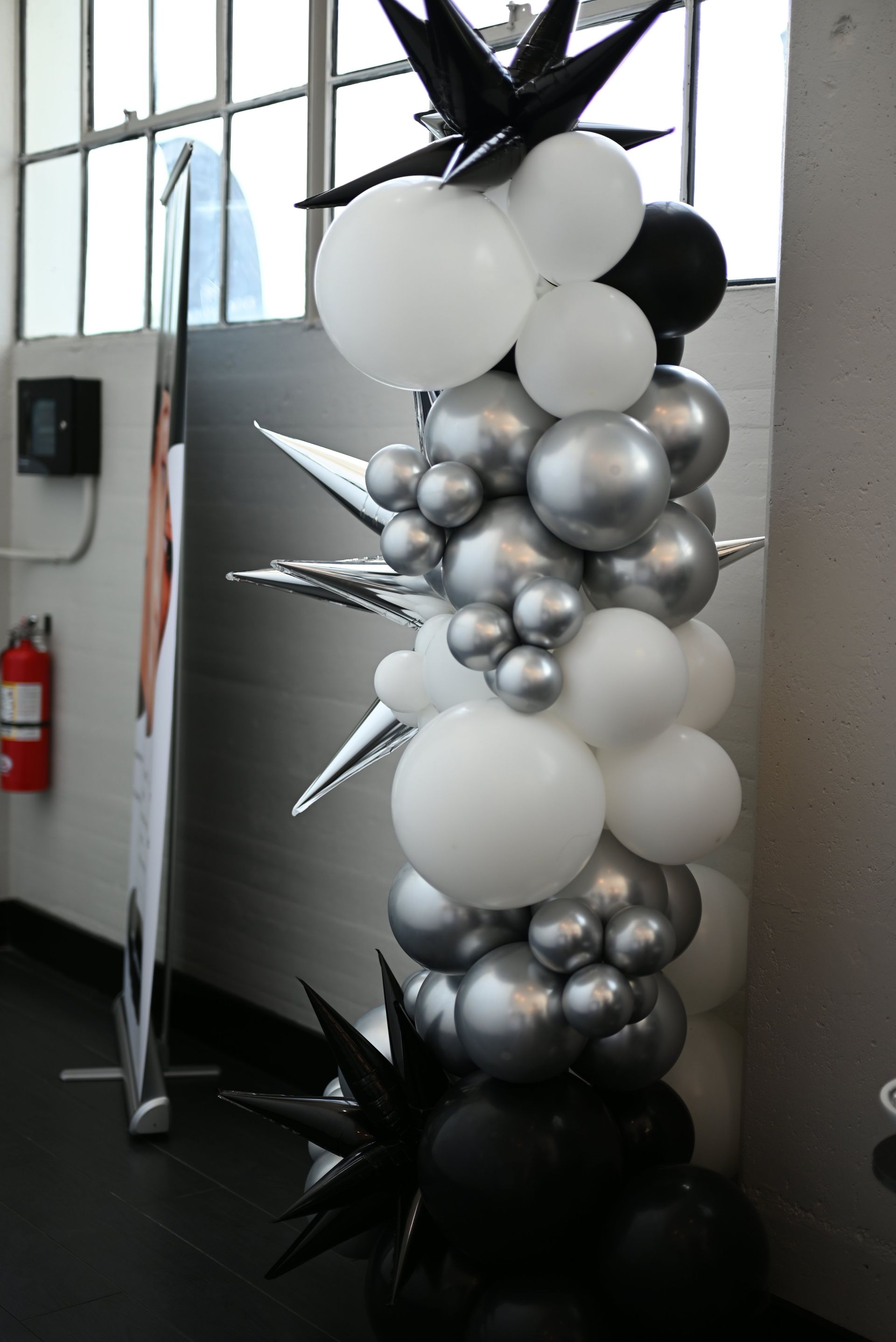 Black, silver, and white balloon column with starburst decorations indoors near a mirror