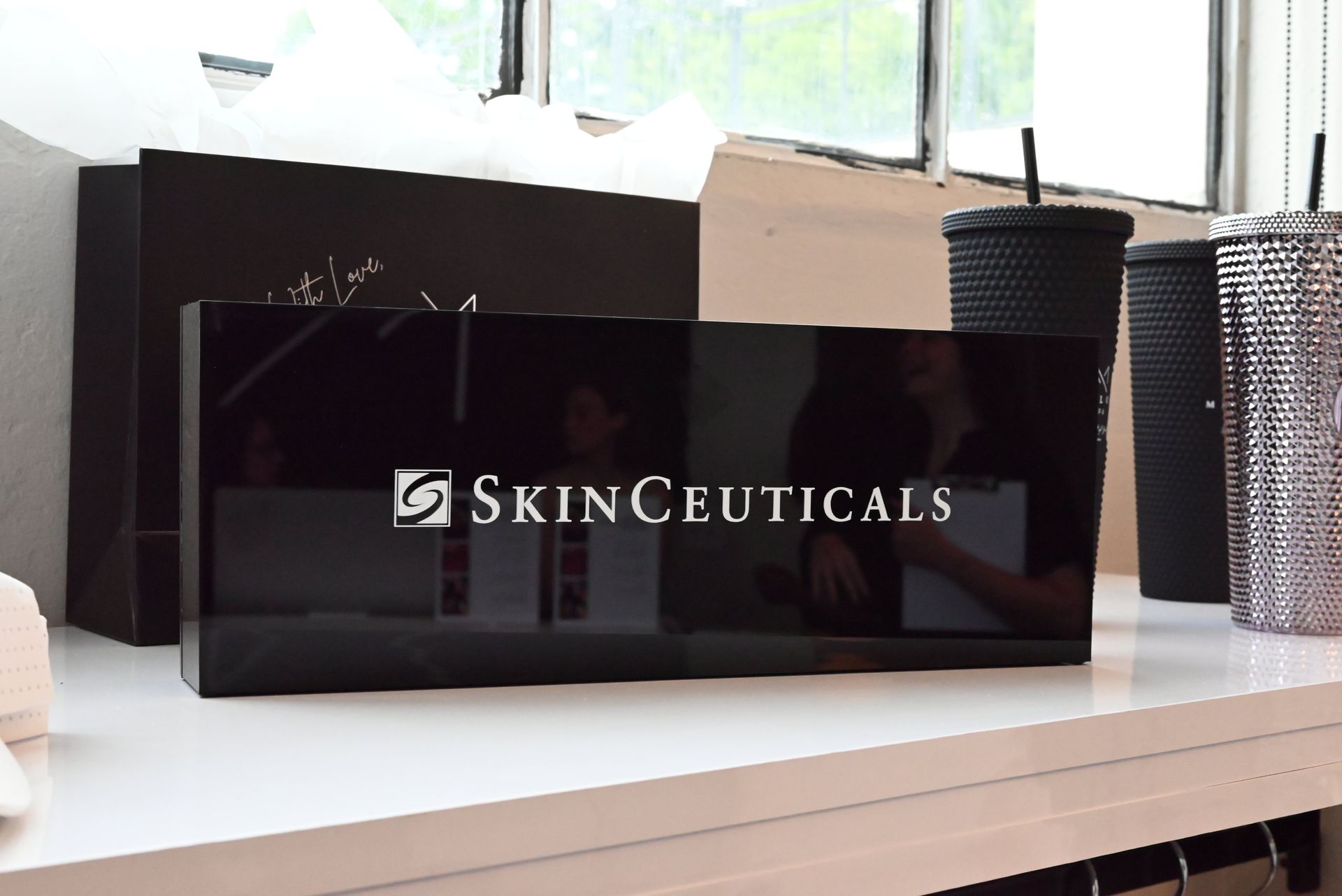 SkinCeuticals black product boxes on a white shelf beside a black cup and woven container