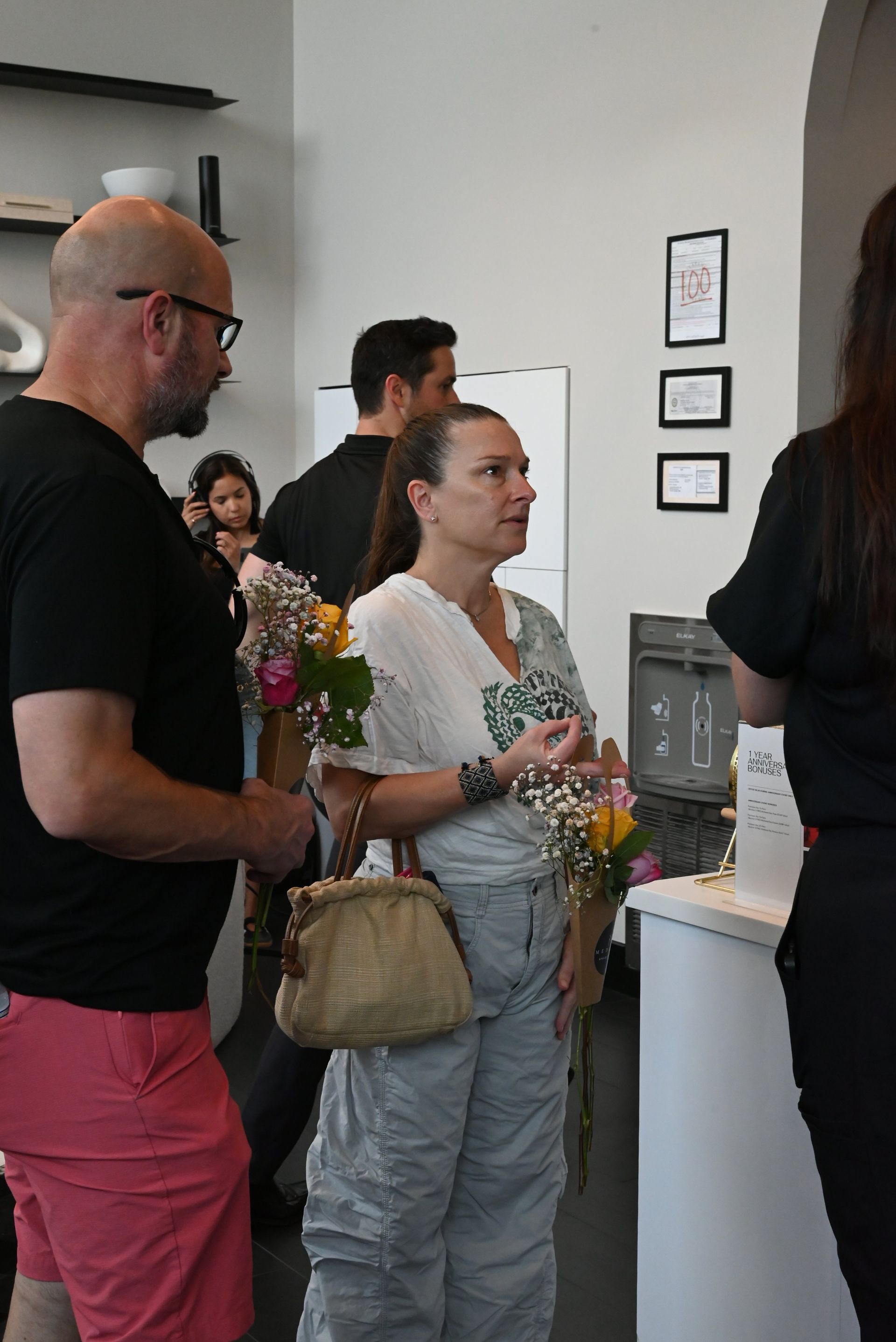 People waiting in line inside a bright shop, holding flowers and tote bags.