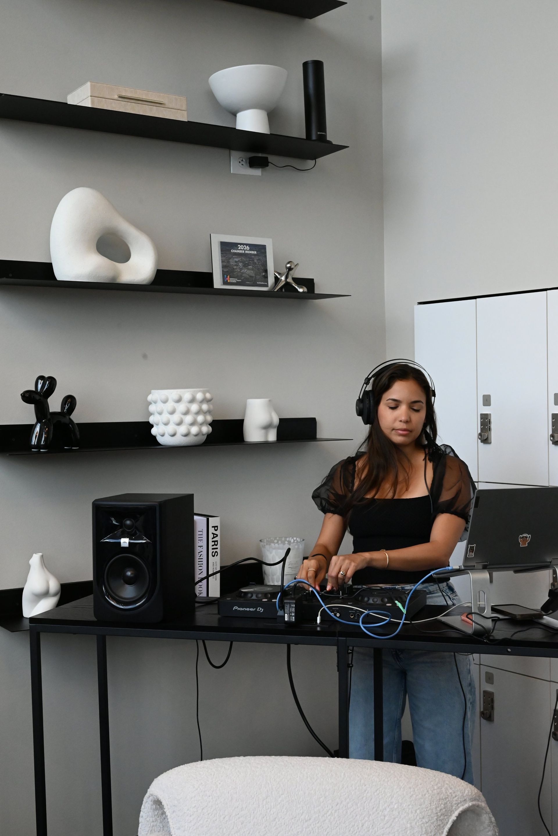 Woman adjusting audio equipment at a desk in a modern studio with shelves and a laptop