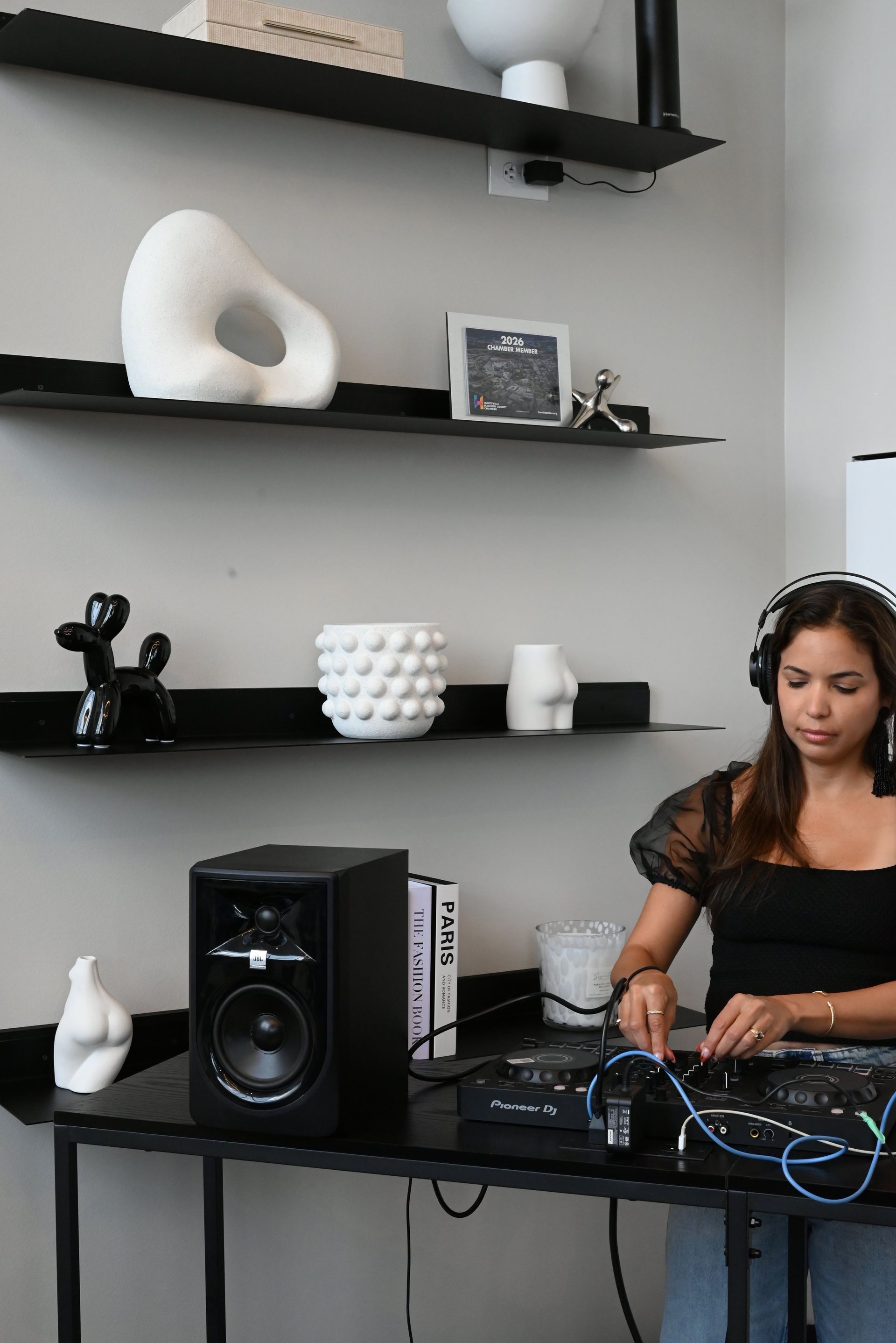 Woman working at a desk with audio equipment and cables in a modern room with floating shelves.