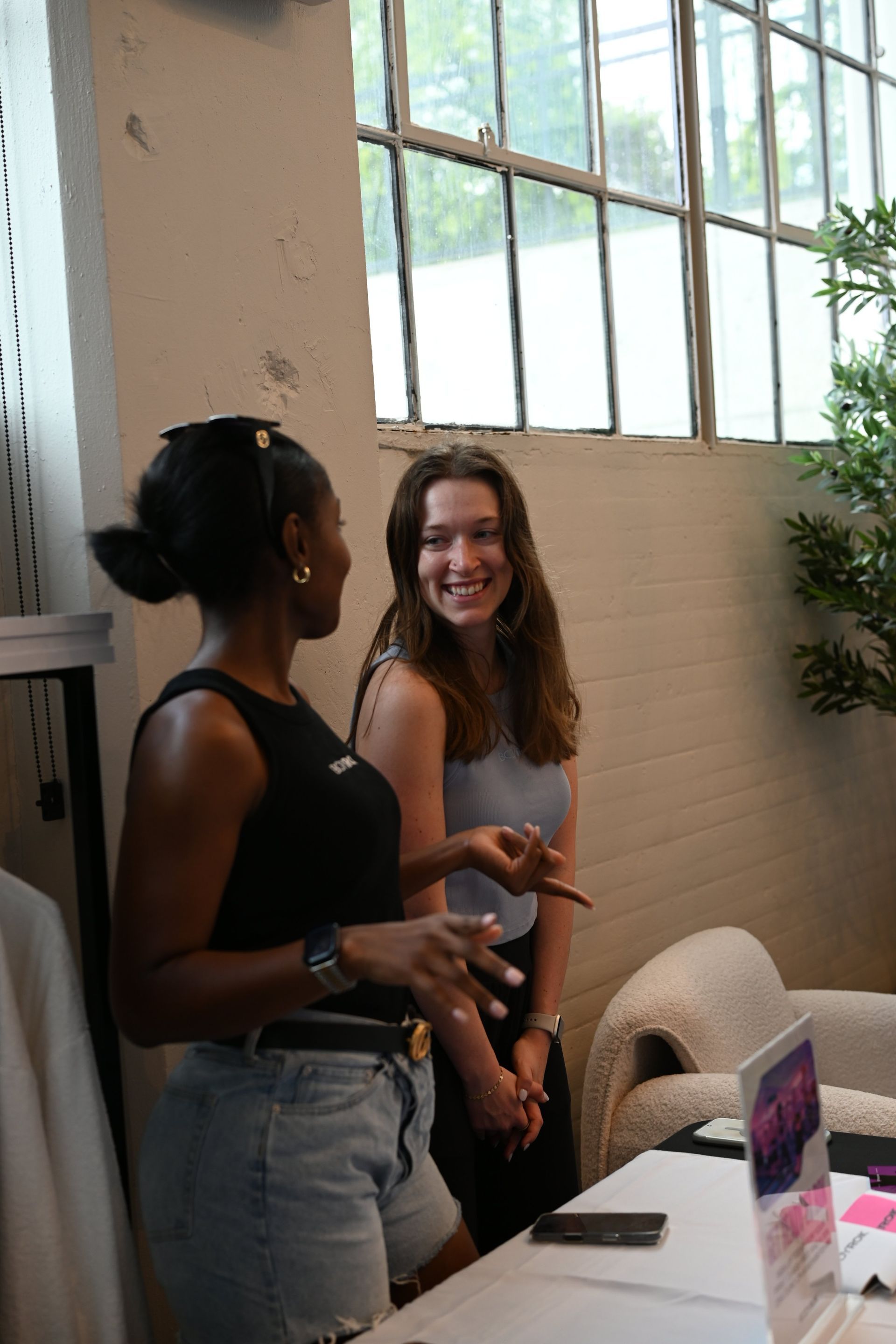 Two people talking beside a table in a bright room with large windows