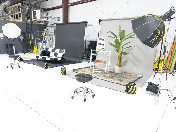 Studio set with backdrop, softbox lights, chair, potted plant, and camera equipment on a white floor