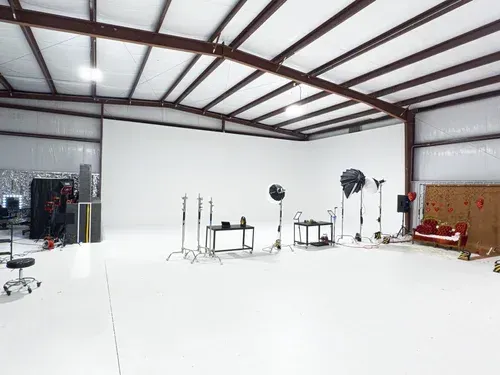 Empty photography studio with white cyclorama wall, lighting stands, and a red couch along the right wall