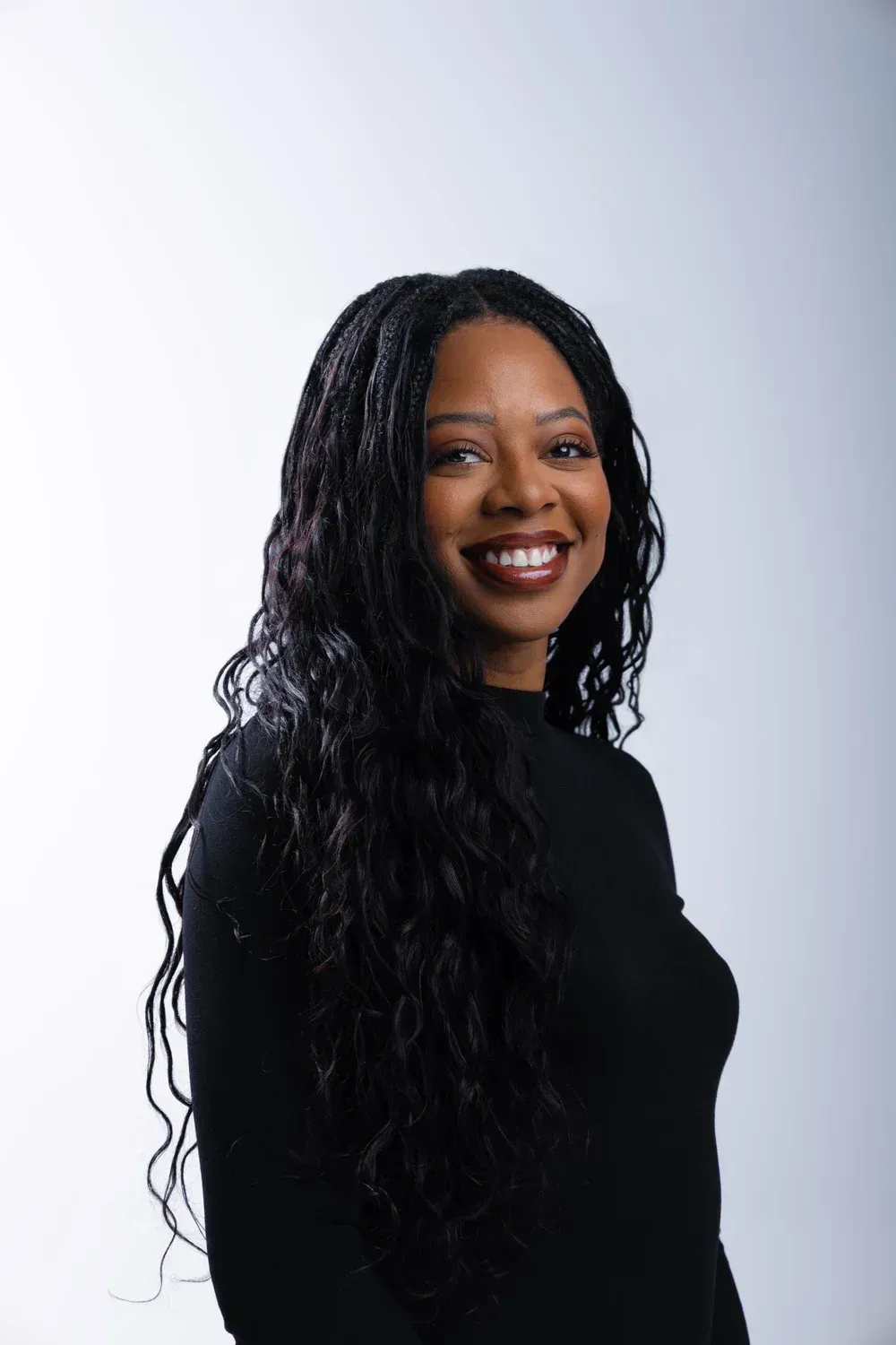 Smiling person with long black hair in a black top against a light gray background