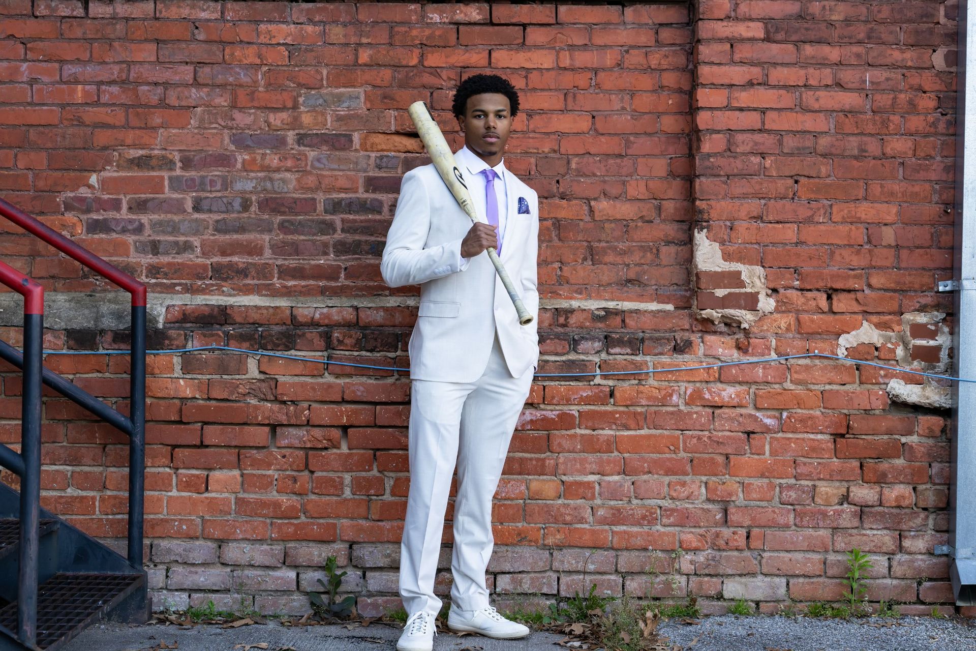 Person in a white suit holding a baseball bat against a brick wall.