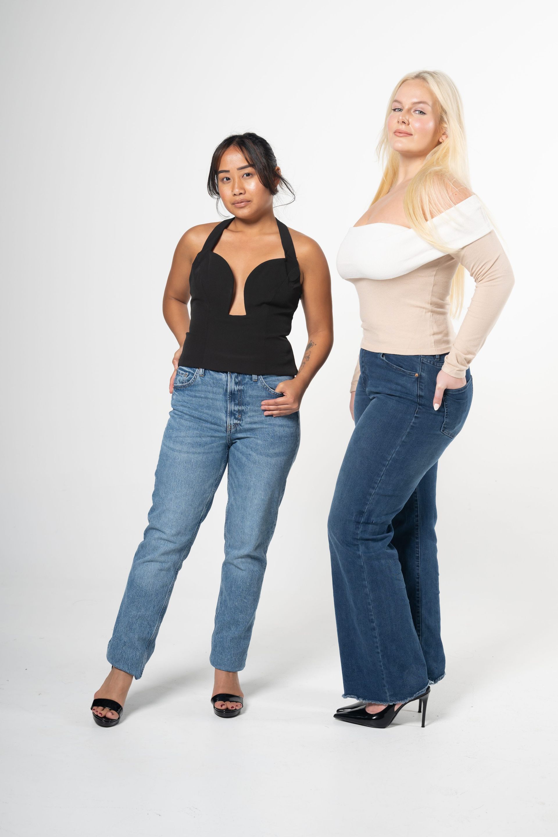 Two women modeling jeans and tops against a white studio backdrop
