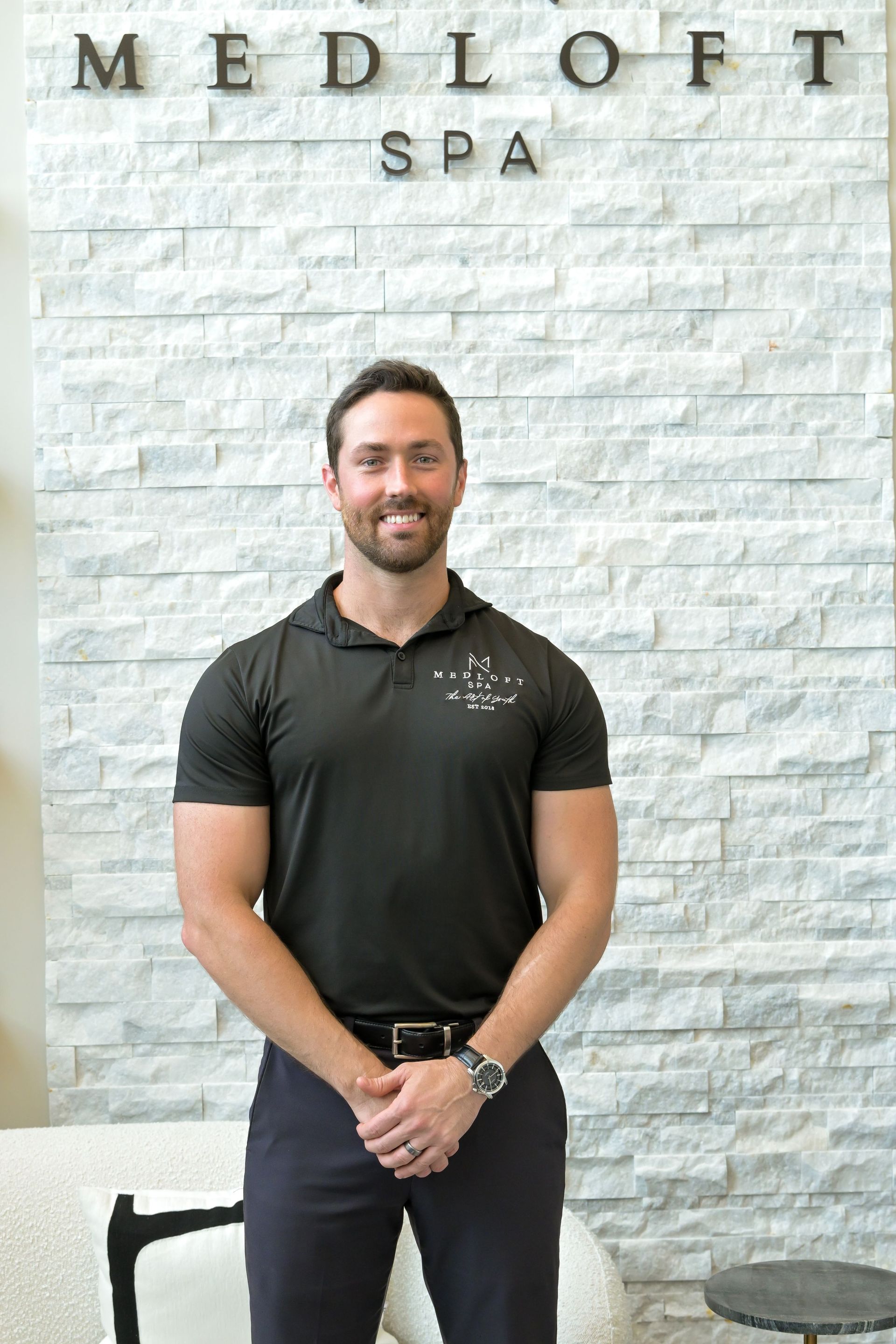 Man standing in front of a Med Loft Spa sign, wearing a black polo and dark pants.