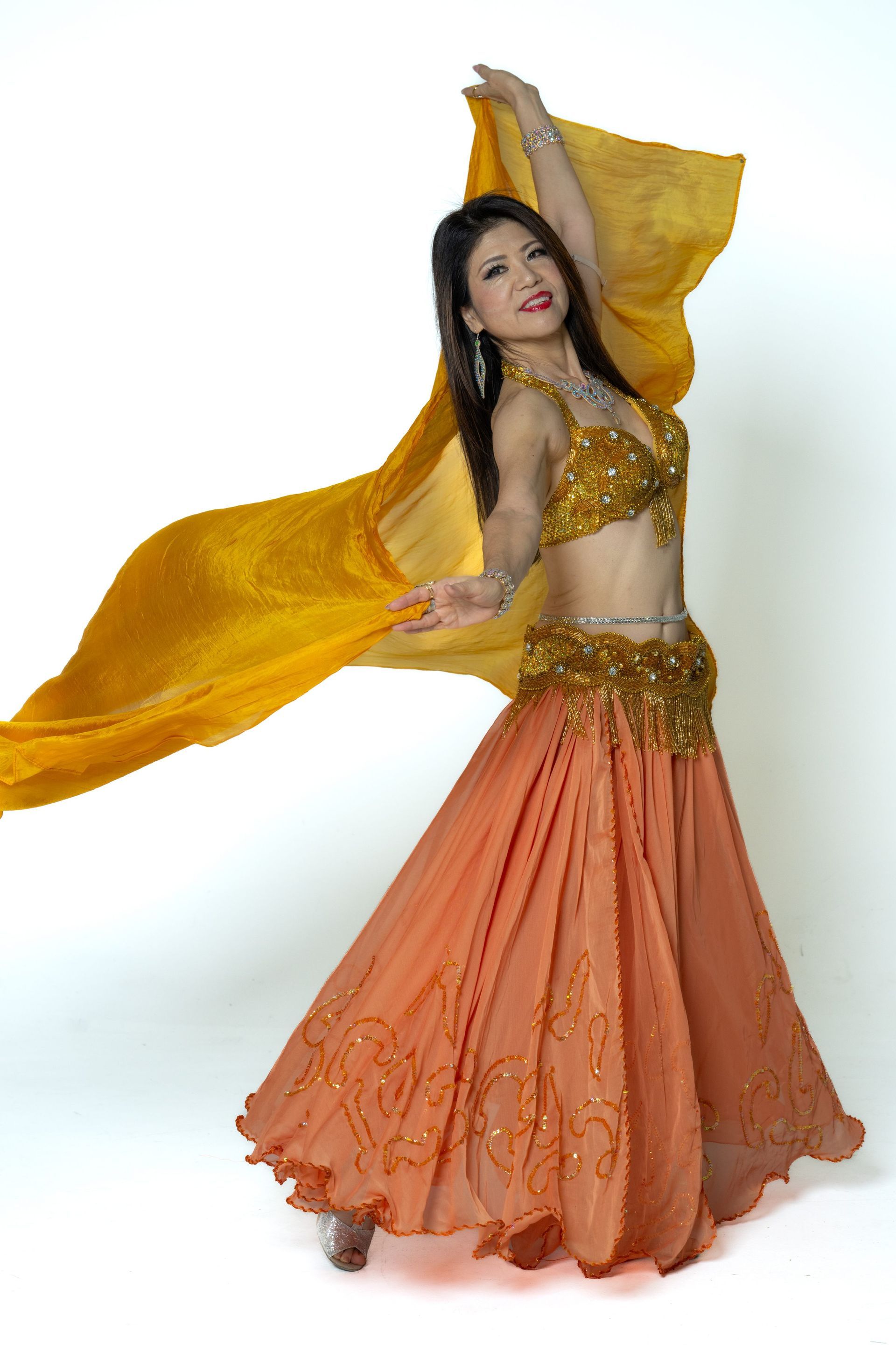 Dancer in gold top and orange skirt twirls with flowing yellow veil on a white background