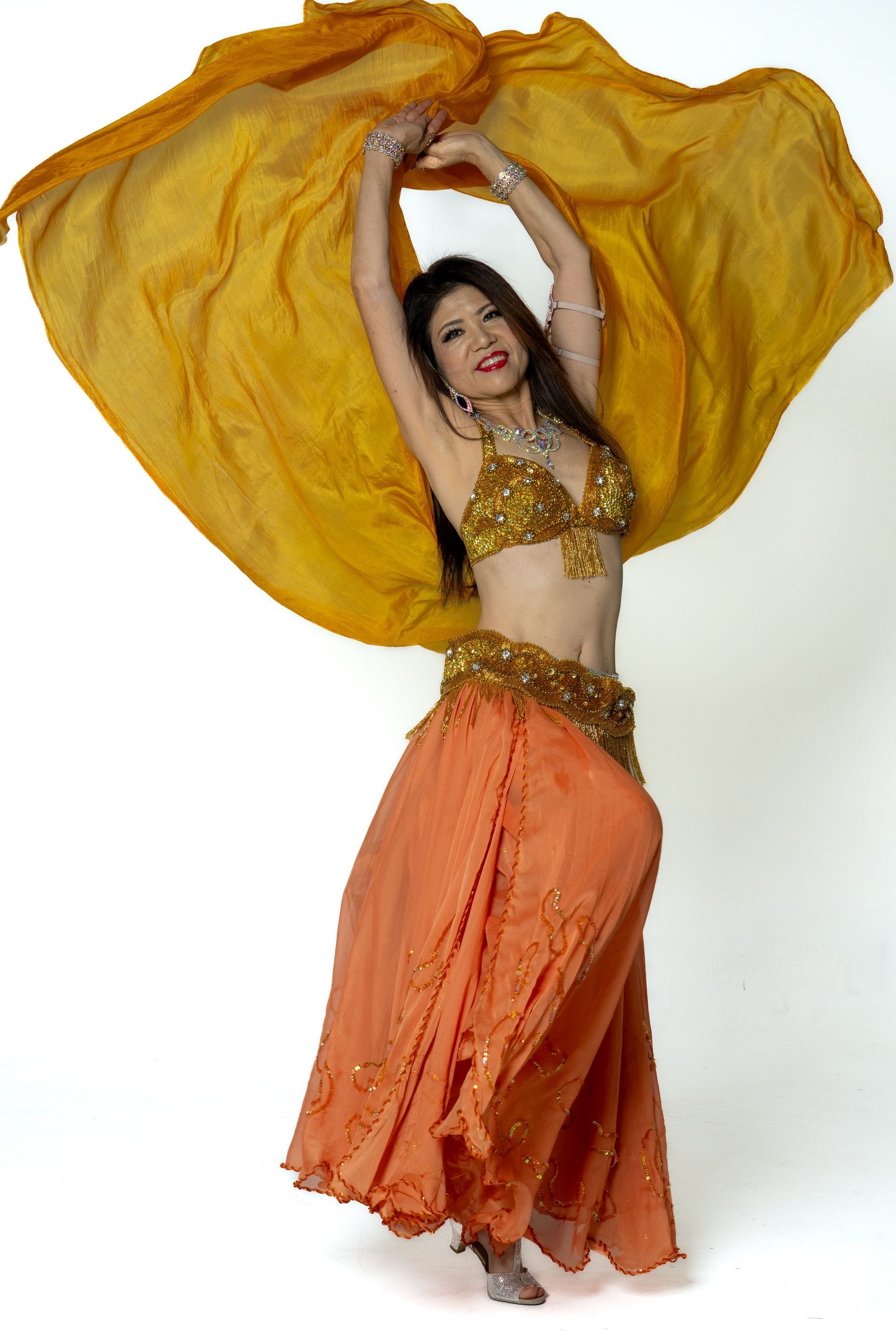 Dancer in gold and orange costume twirling with flowing yellow fabric against a white background