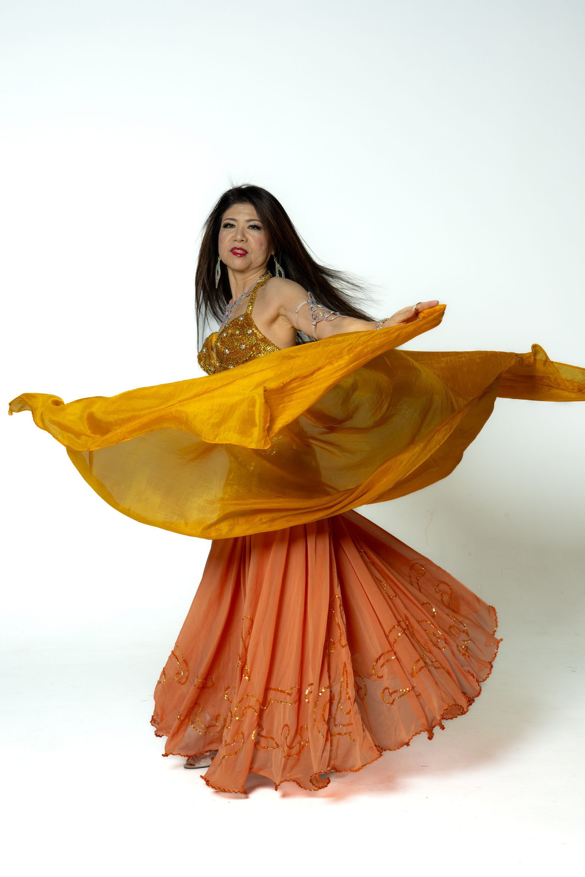 Woman dancing in a flowing yellow shawl and orange skirt against a white background