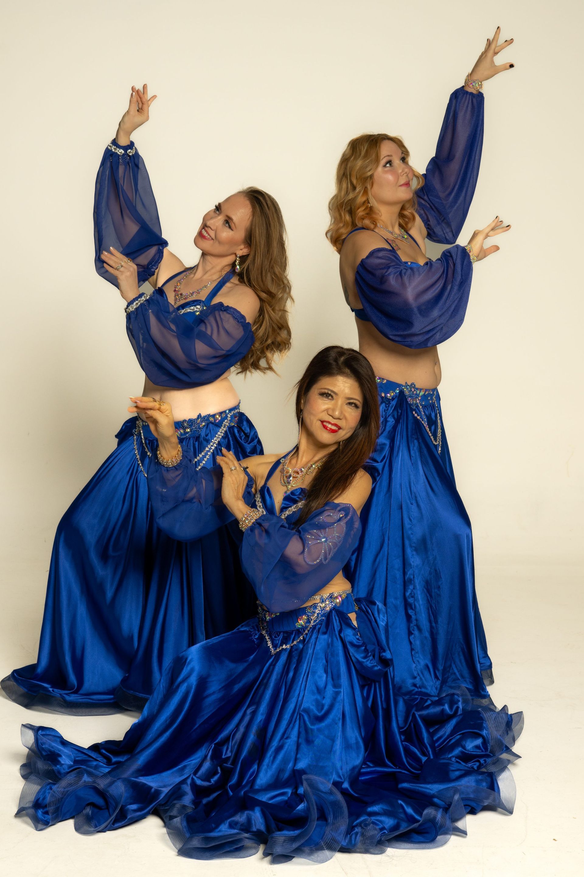 Three dancers in blue costumes pose gracefully against a light background.