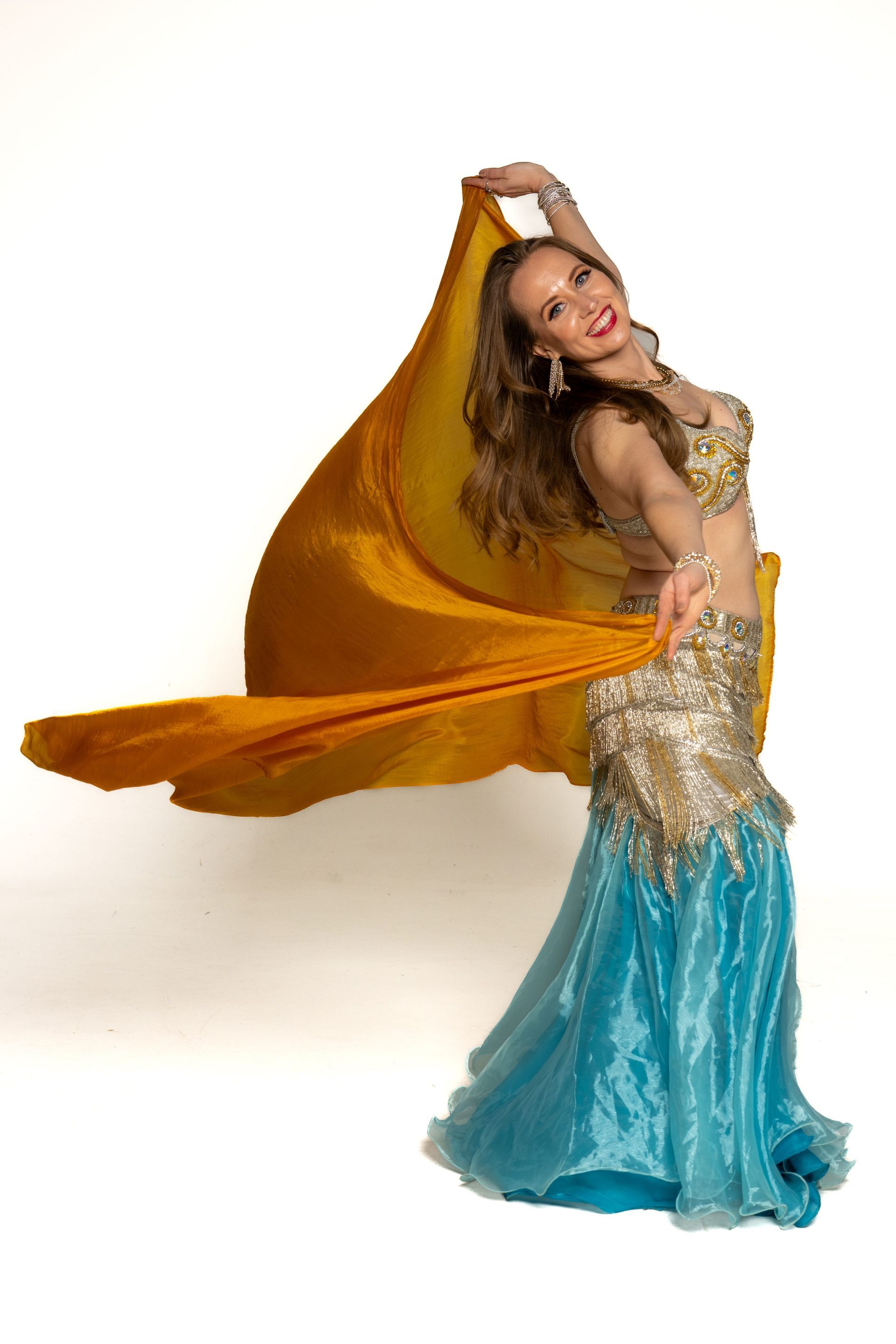 Dancer in gold and turquoise costume with orange veil, posing against a white background