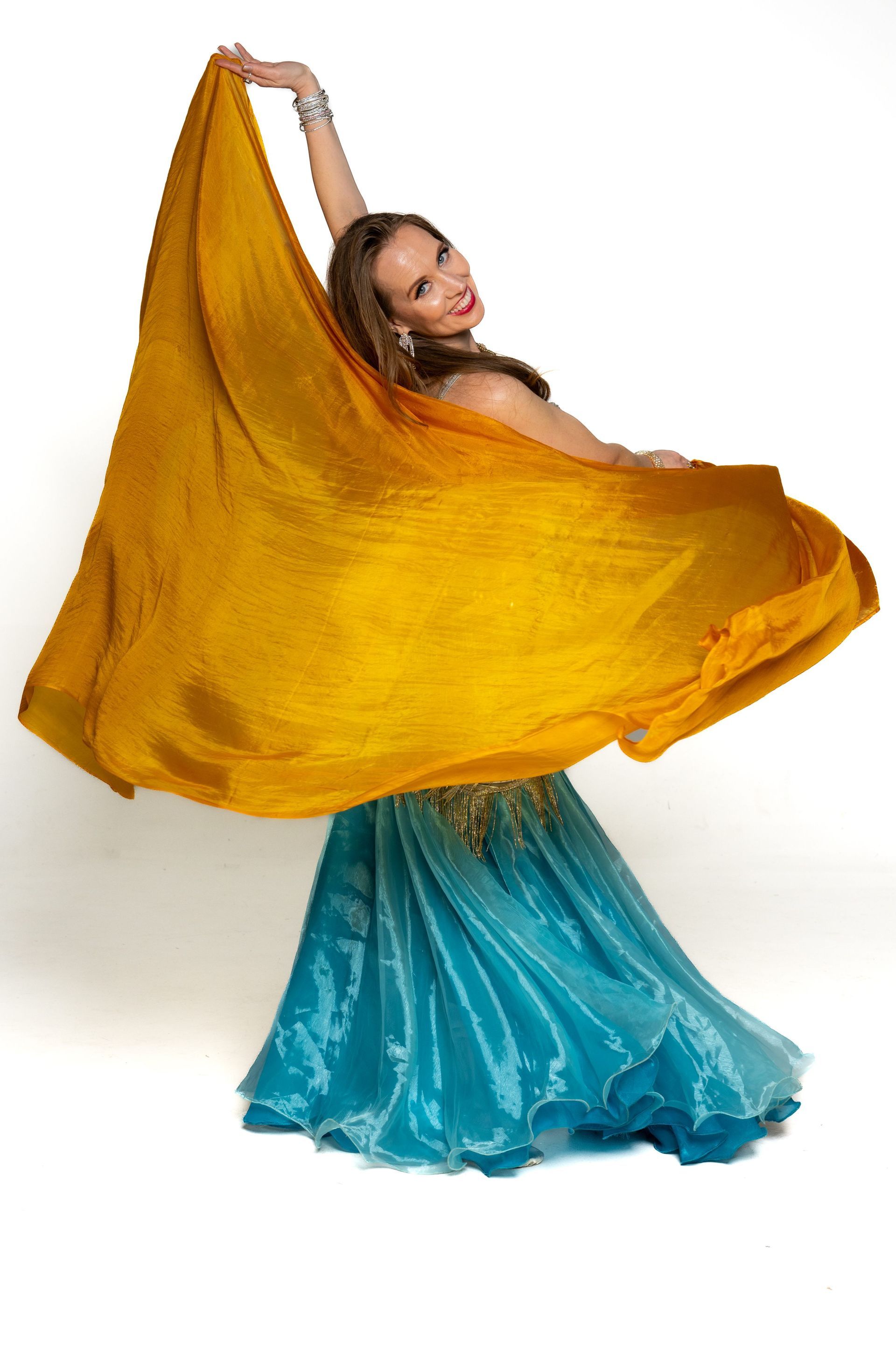 Dancer twirls with a flowing gold veil and turquoise skirt against a white background