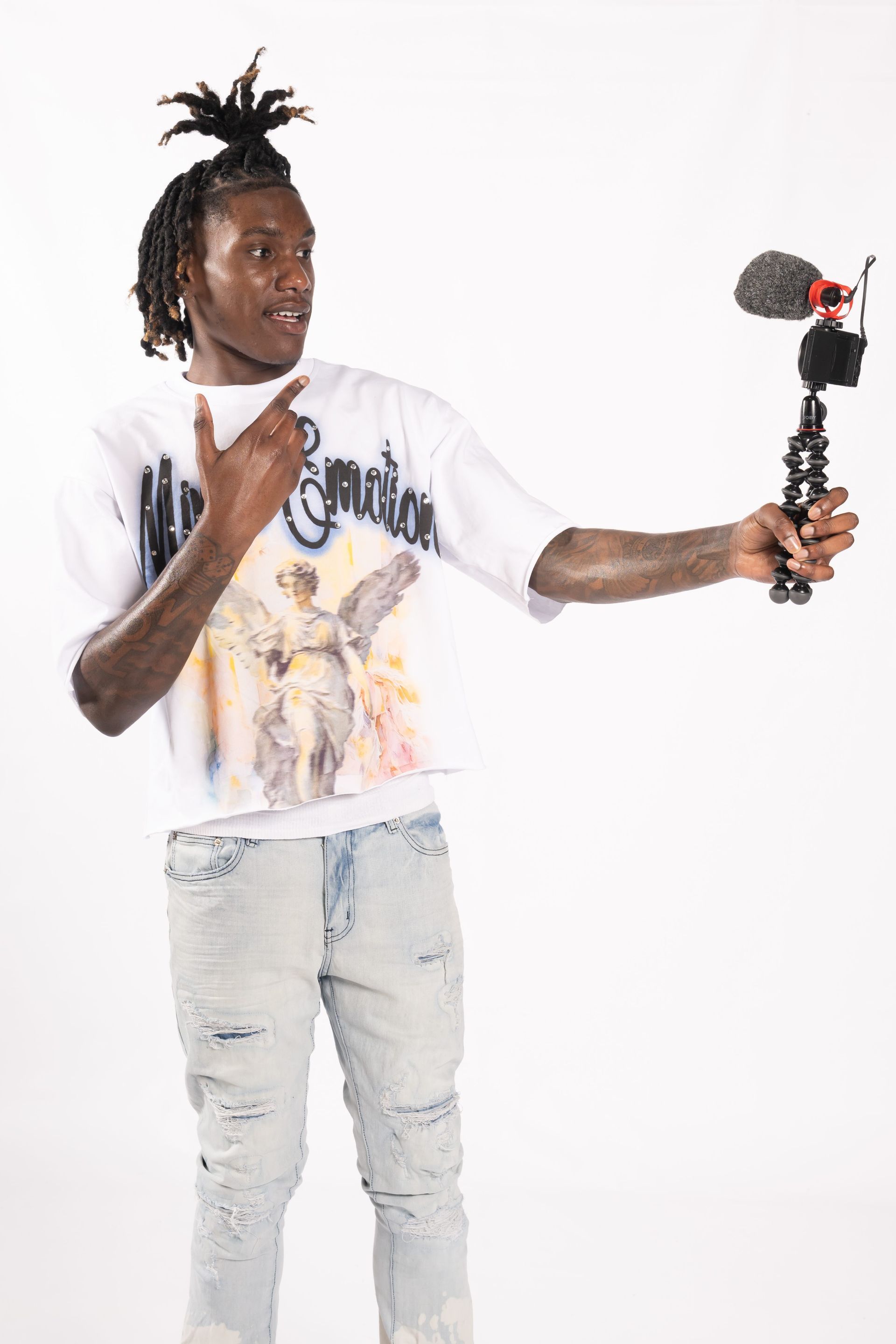 Person in a white graphic T-shirt and ripped jeans holds out a small camera rig against a white background.
