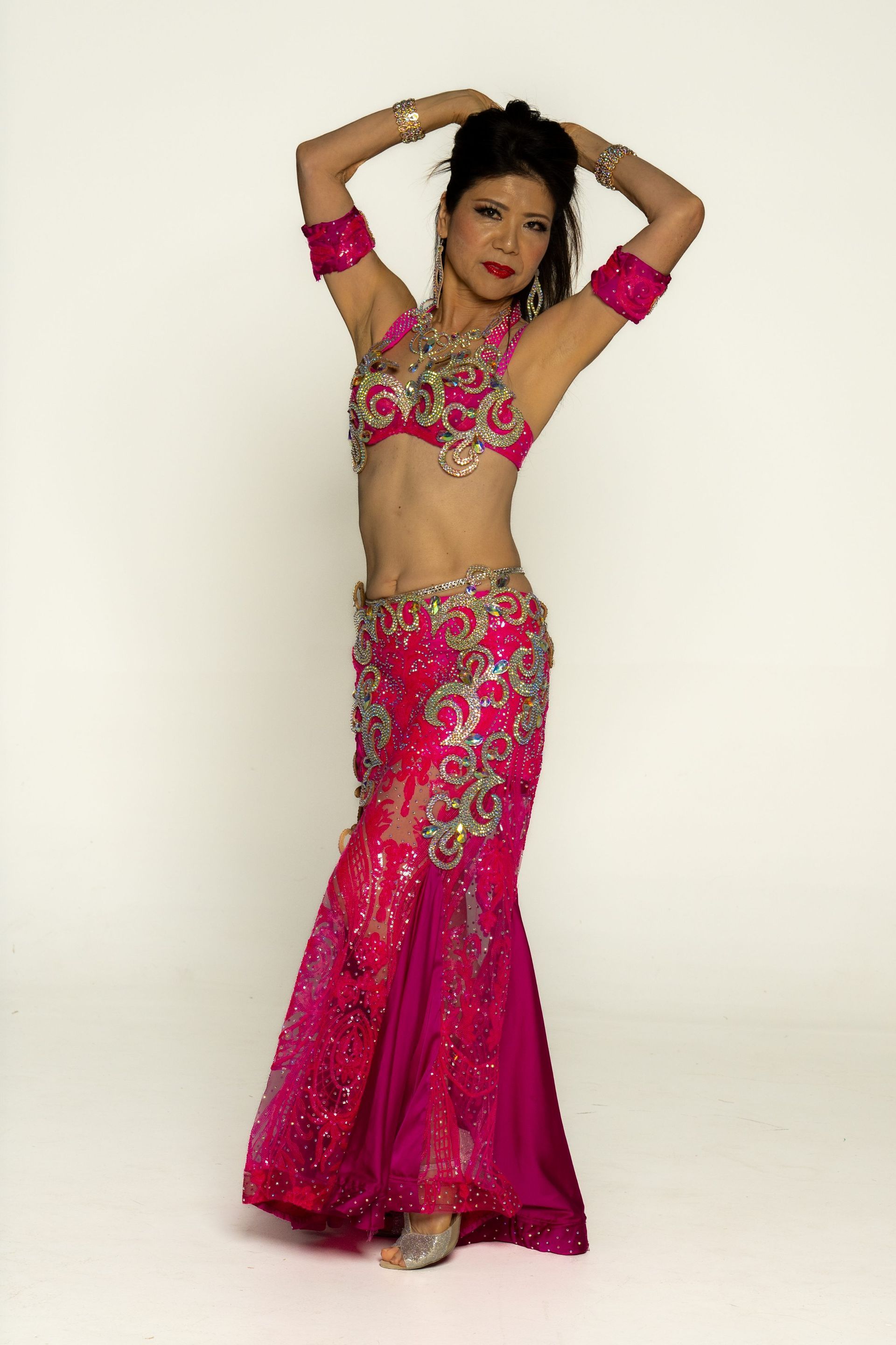 Woman in a bright pink embellished dance costume posing with arms raised against a plain background