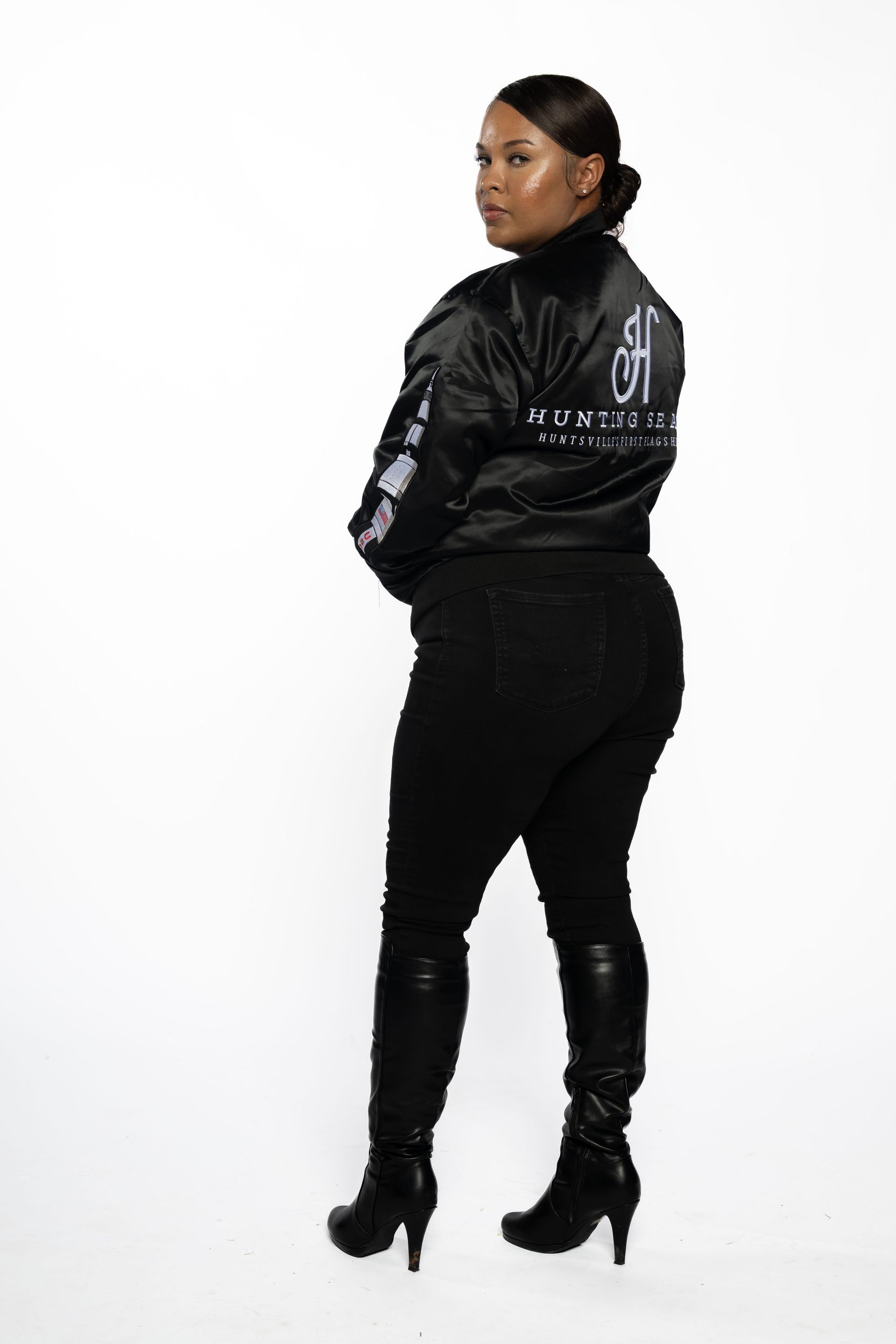 Person in black jacket, pants, and boots, standing turned away on a plain white background.