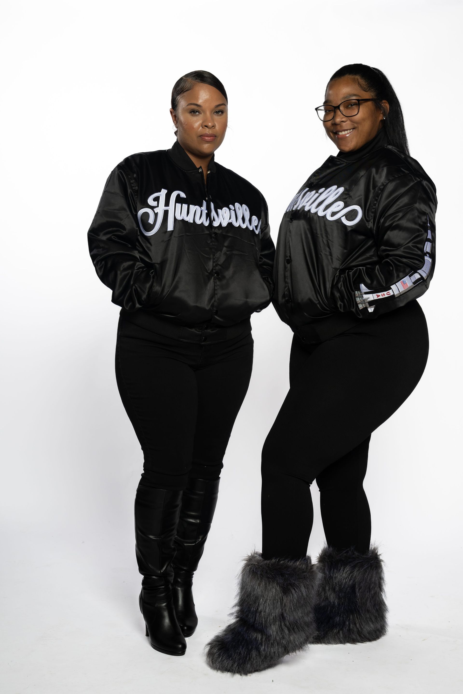 Two people in matching black graphic jackets and black pants pose against a white background.