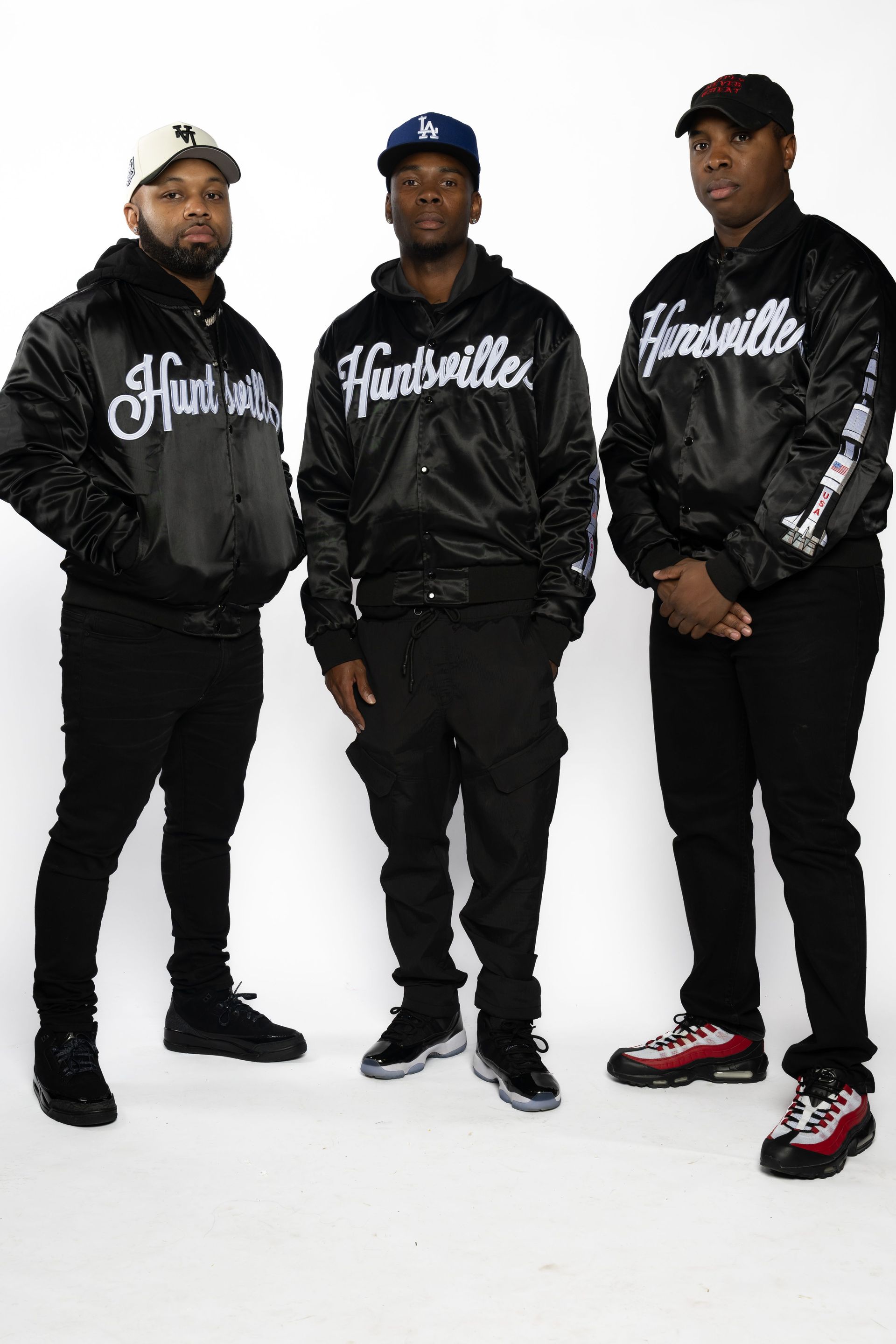 Three men in black Hoodville hoodies and caps posing against a white background.