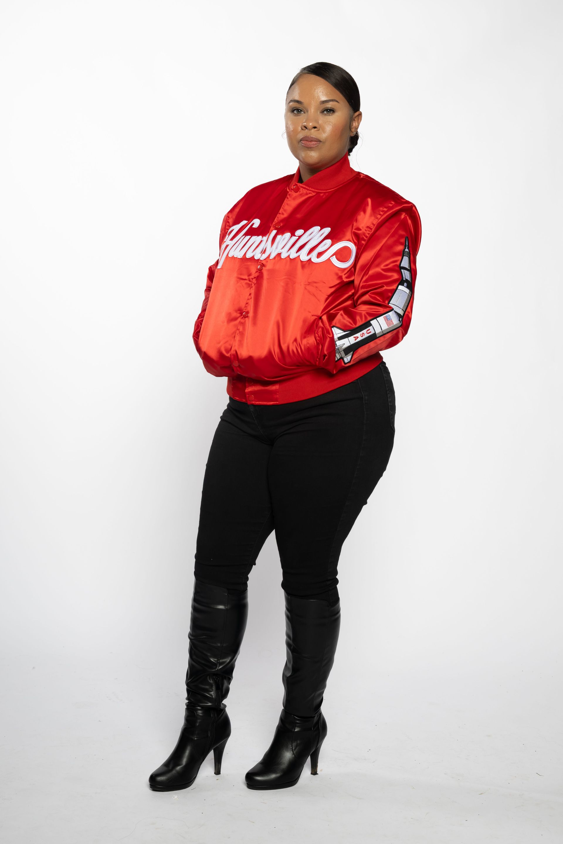 Person standing in a red satin jacket, black pants, and black boots against a white background