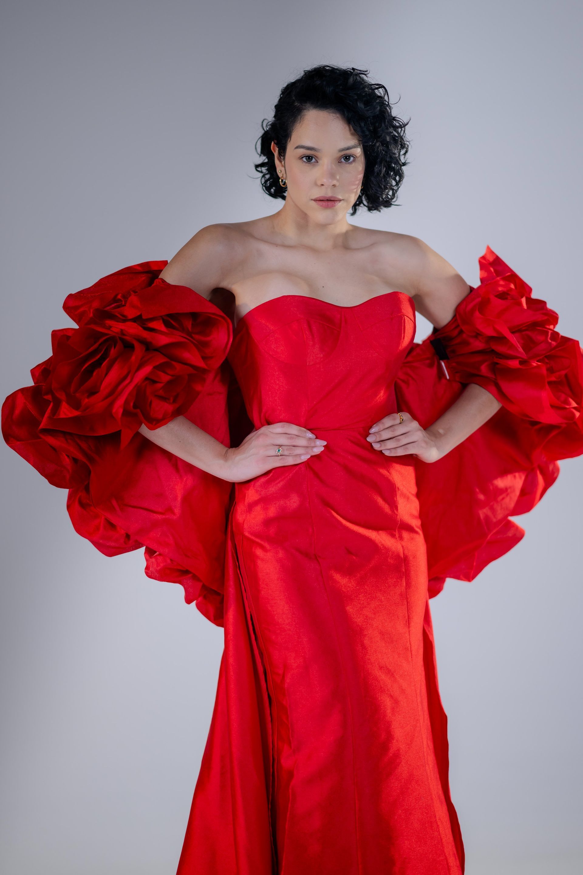 Person in a bright red, ruffled off-shoulder gown posing against a gray background